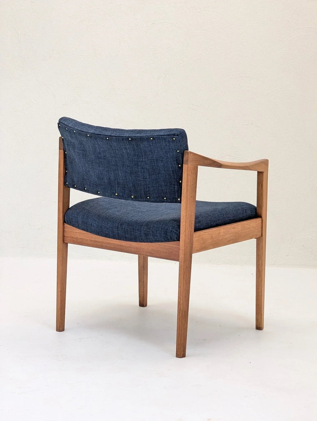 Mid-century modern wooden armchair with blue upholstered seat and backrest, minimalist setting
