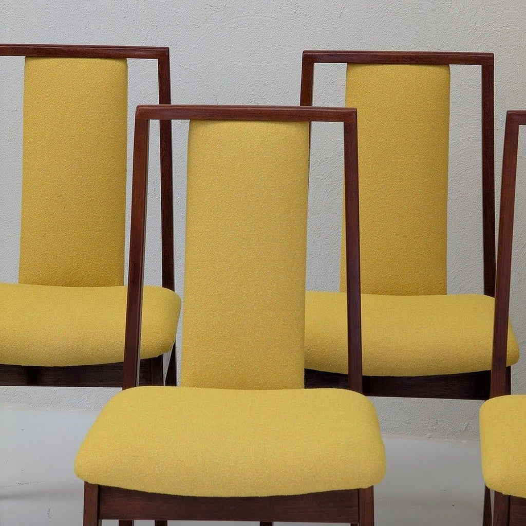 Mid-century modern dining chairs with yellow upholstery and wooden frames against a light wall