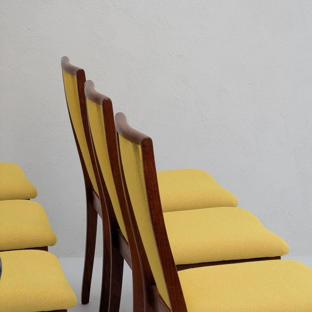 Mid-century modern dining chairs with yellow upholstery and wooden frames against a white wall.