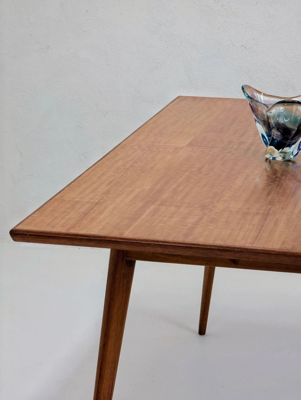 Mid-century modern golden teak dining table with angled legs, glass bowl centerpiece