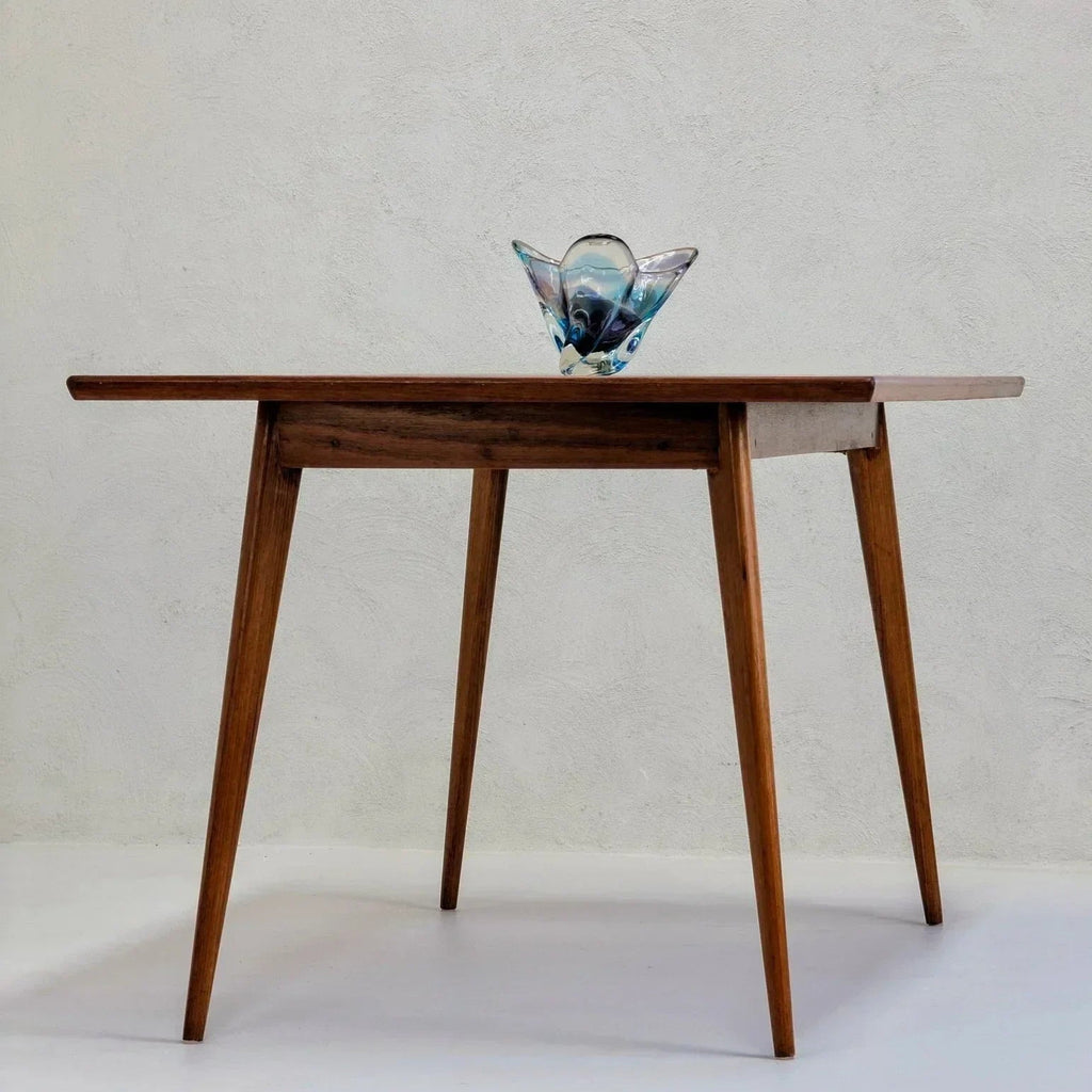 Mid-century modern golden teak dining table with glass decor against a plain wall