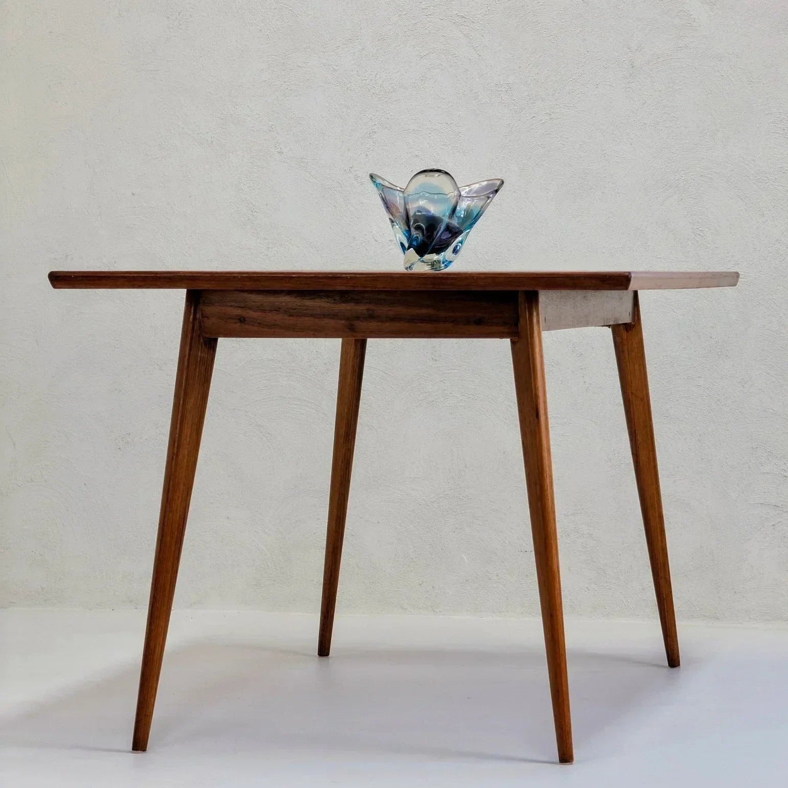 Mid-century modern golden teak dining table with glass decor against a plain wall