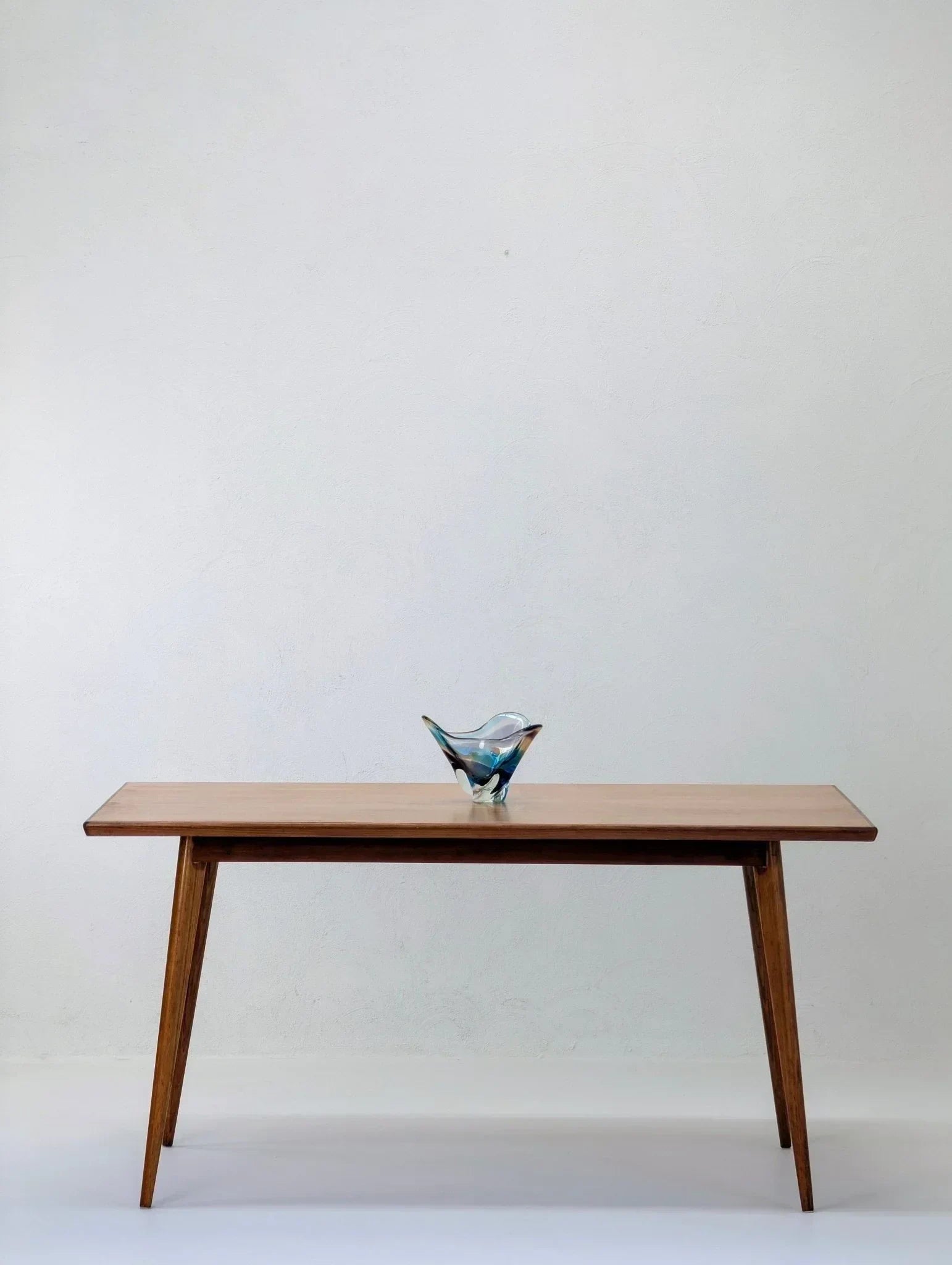 Mid-century modern dining table in golden teak with a decorative glass bowl on top