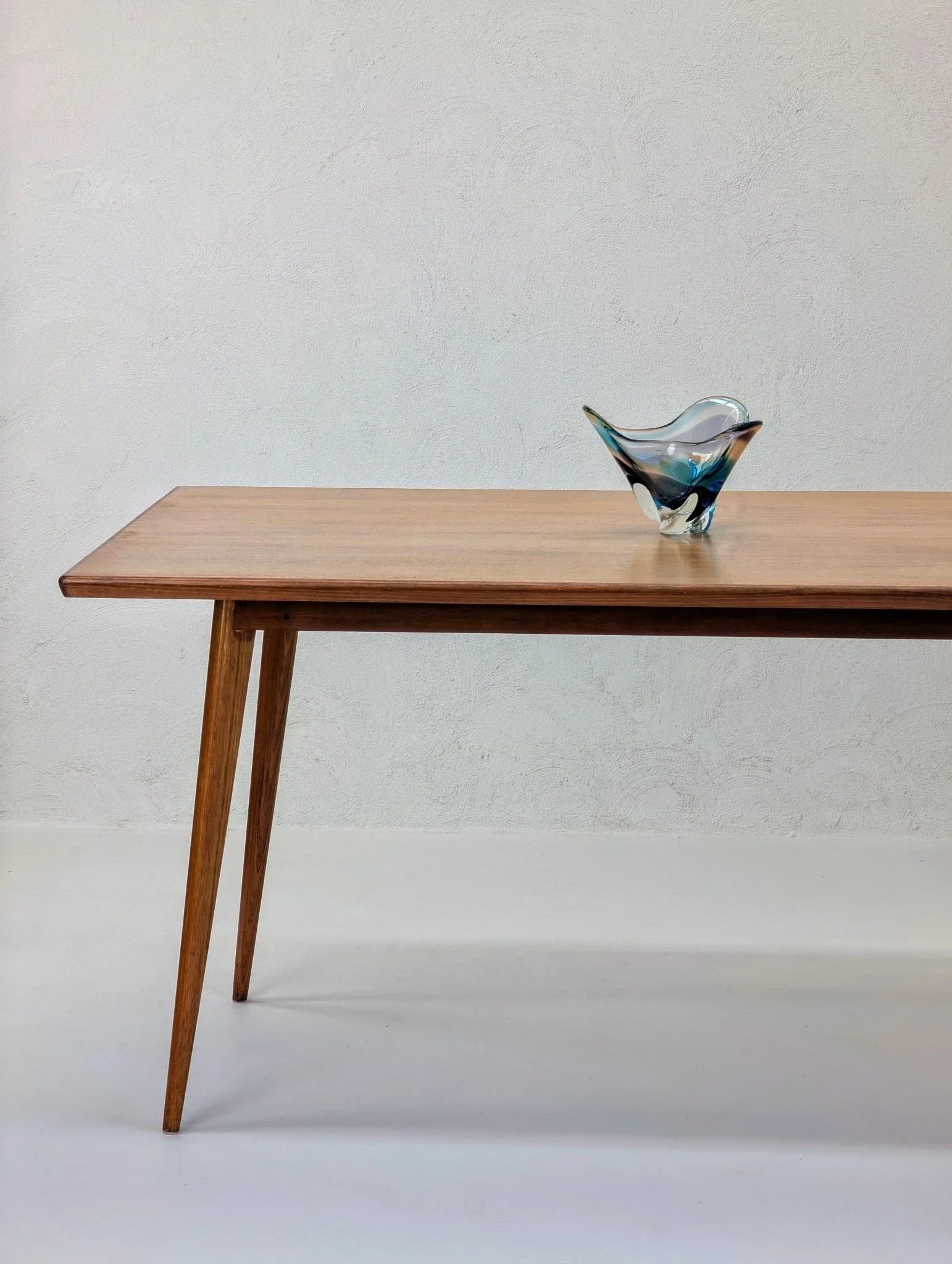 Mid-century modern dining table in golden teak with glass centerpiece on white background