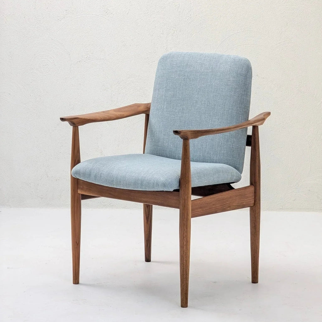 Mid-century modern teak armchair with light blue upholstery against a plain wall