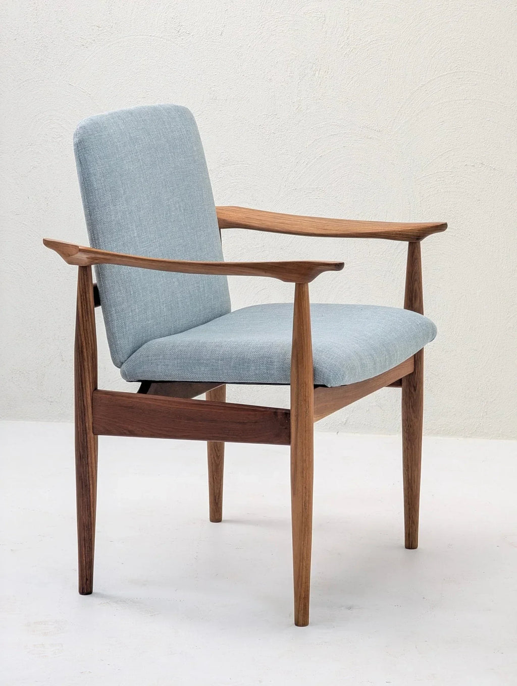 Mid-century modern teak armchair with light blue upholstery on white background