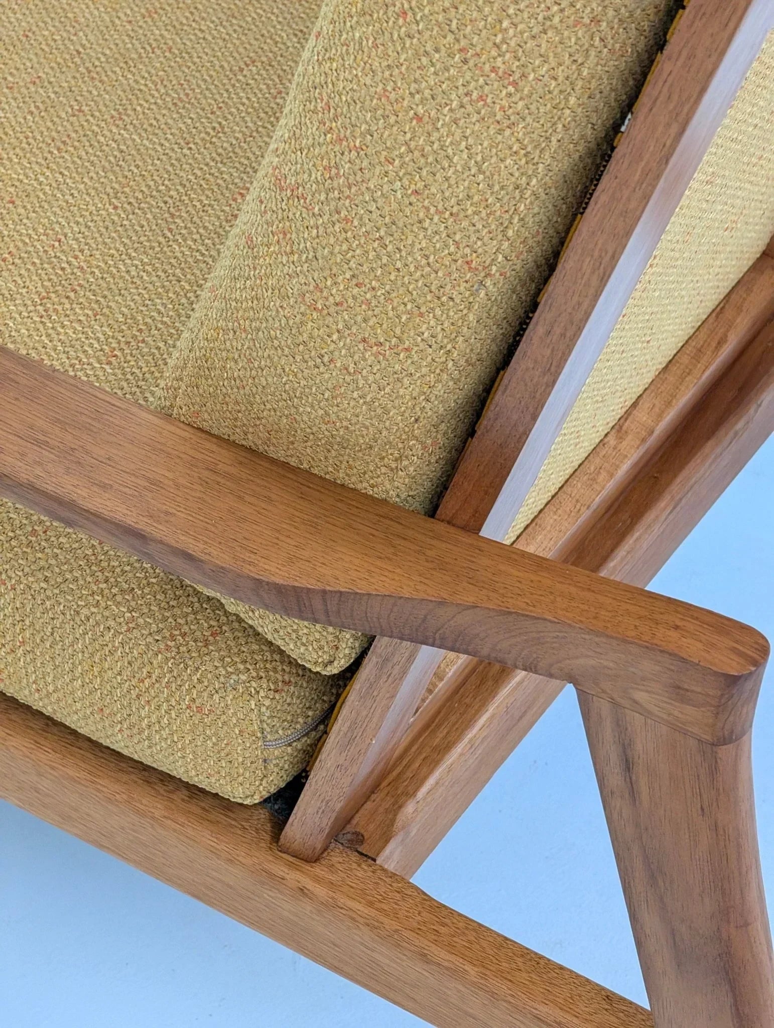 Mid-century modern solid teak lounge chair with tan textured upholstery, close-up view