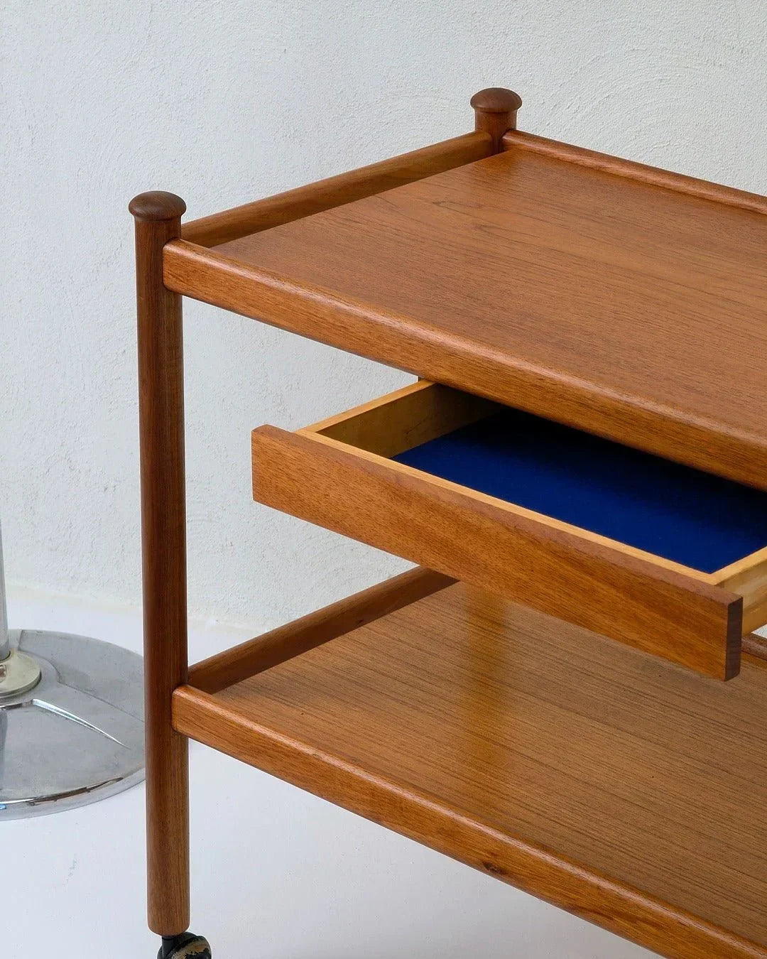 Mid-century teak bar cart with open blue-lined drawer and metal base on wheels