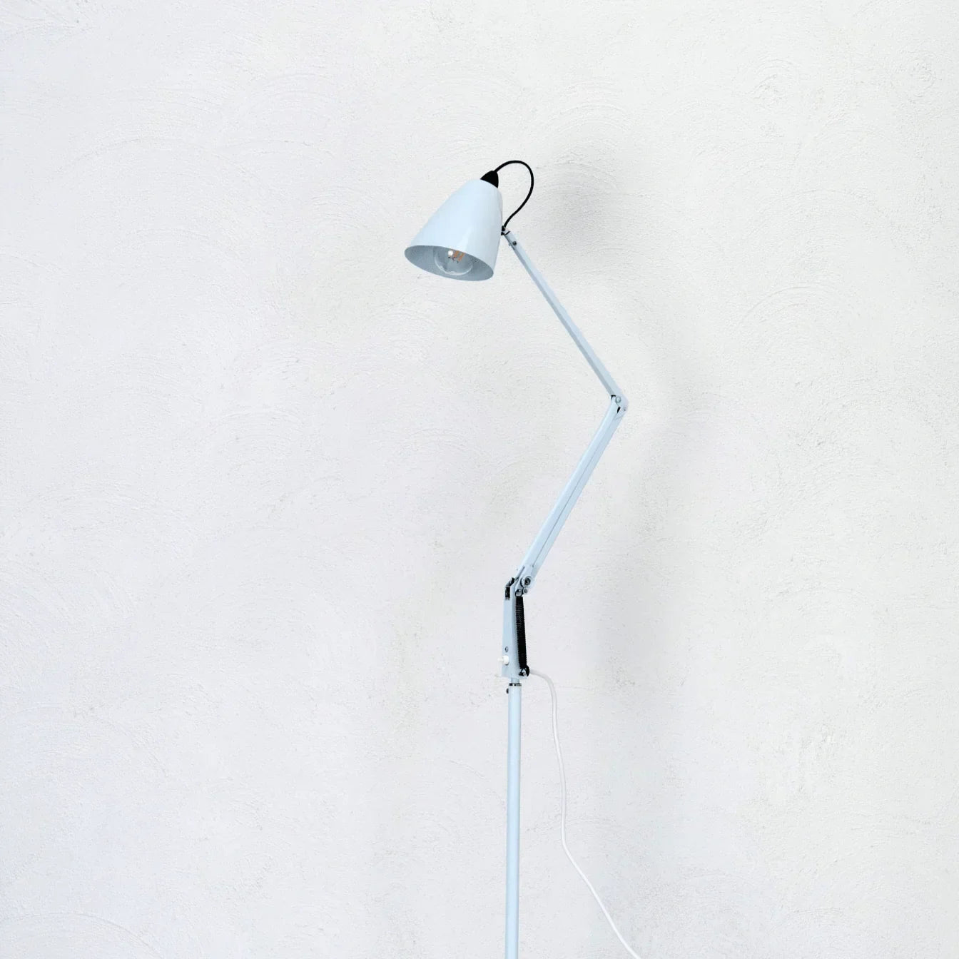 Mid-century modern white studio adjustable floor lamp against a textured white wall
