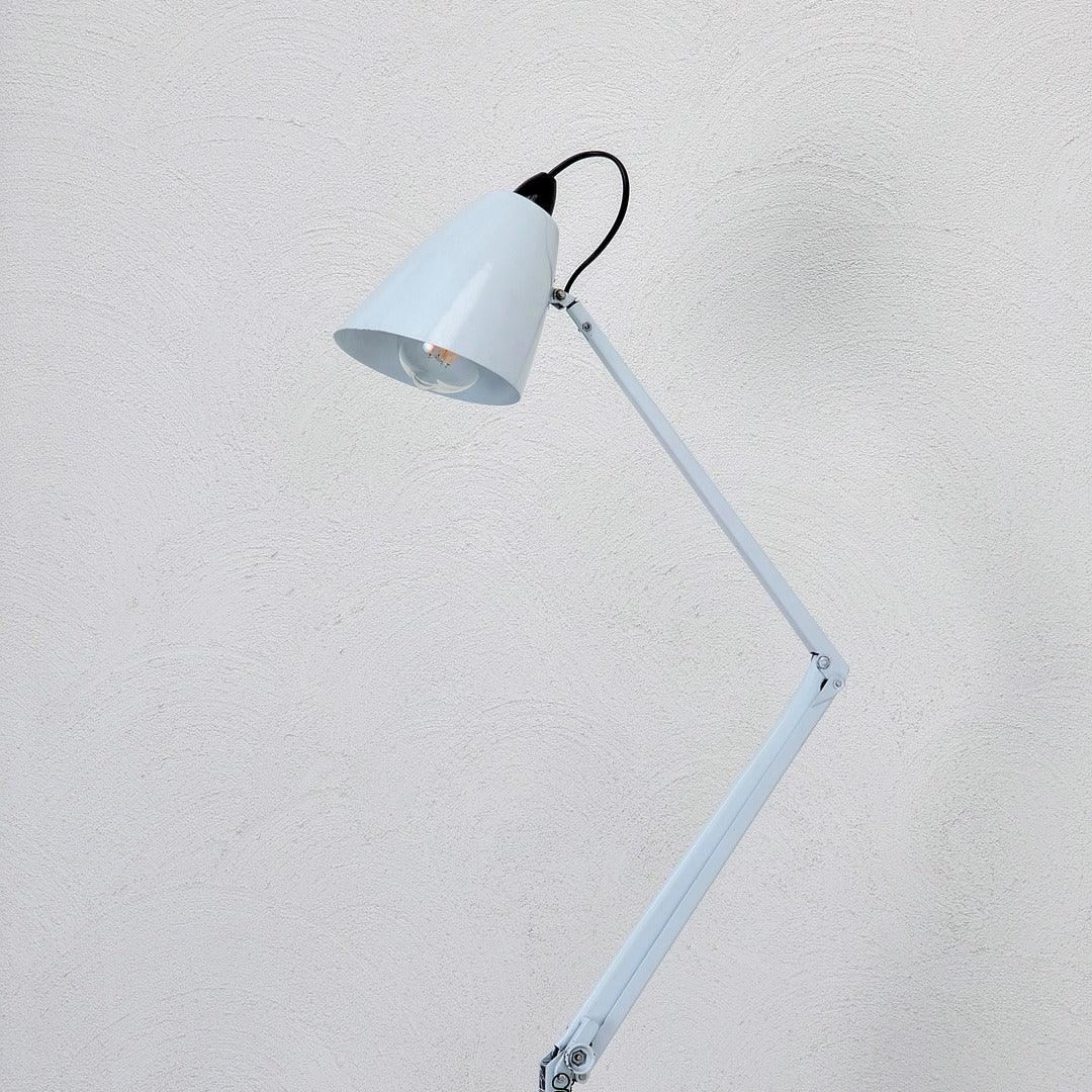 Mid-century white adjustable studio floor lamp with conical shade against a textured wall