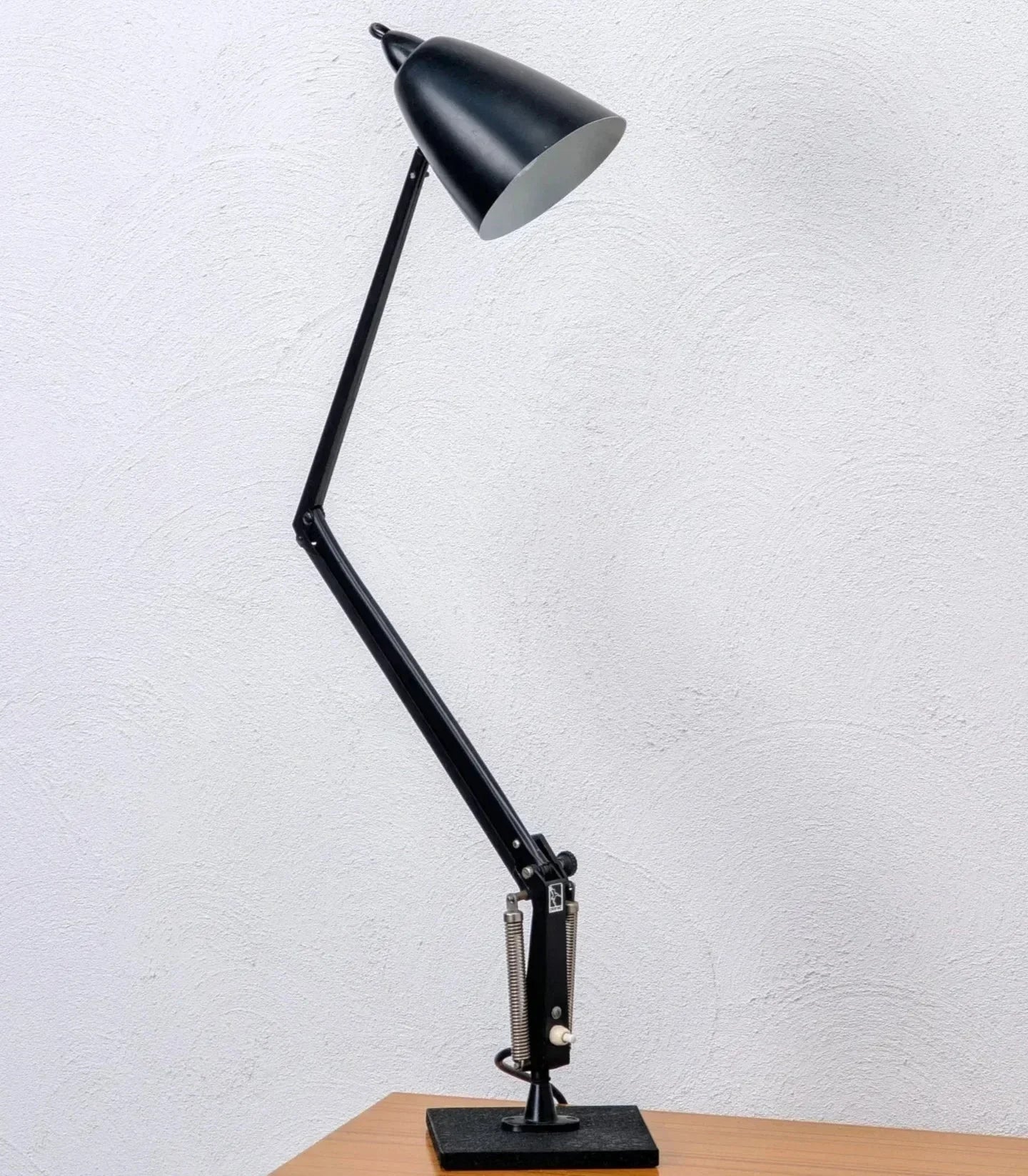 Mid-century black adjustable studio task lamp on a wooden desk against a white wall
