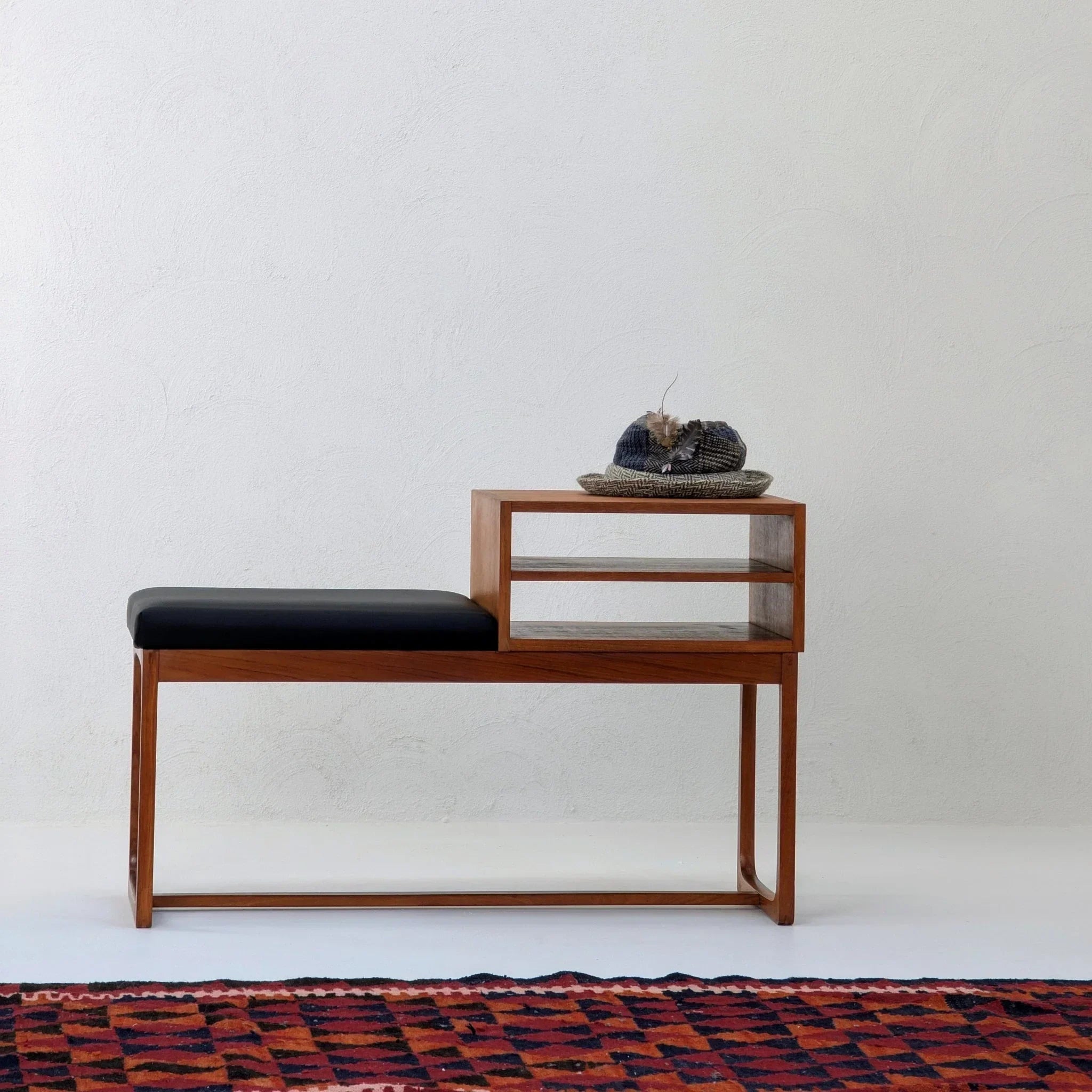 Mid-century teak telephone table with black seat, shelf, hat and red patterned rug