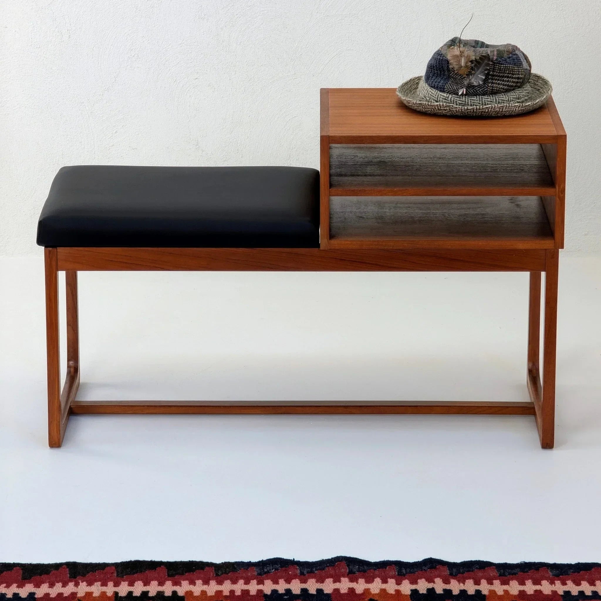 Mid-century teak telephone table with black seat, shelves, and a woven hat on top