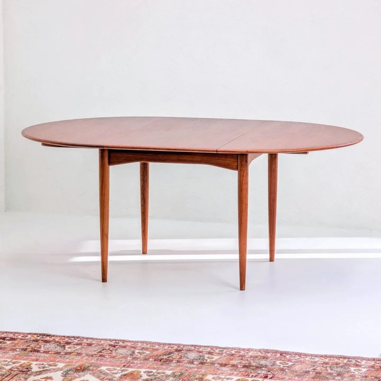 Mid-century modern teak extension dining table on white floor with patterned rug