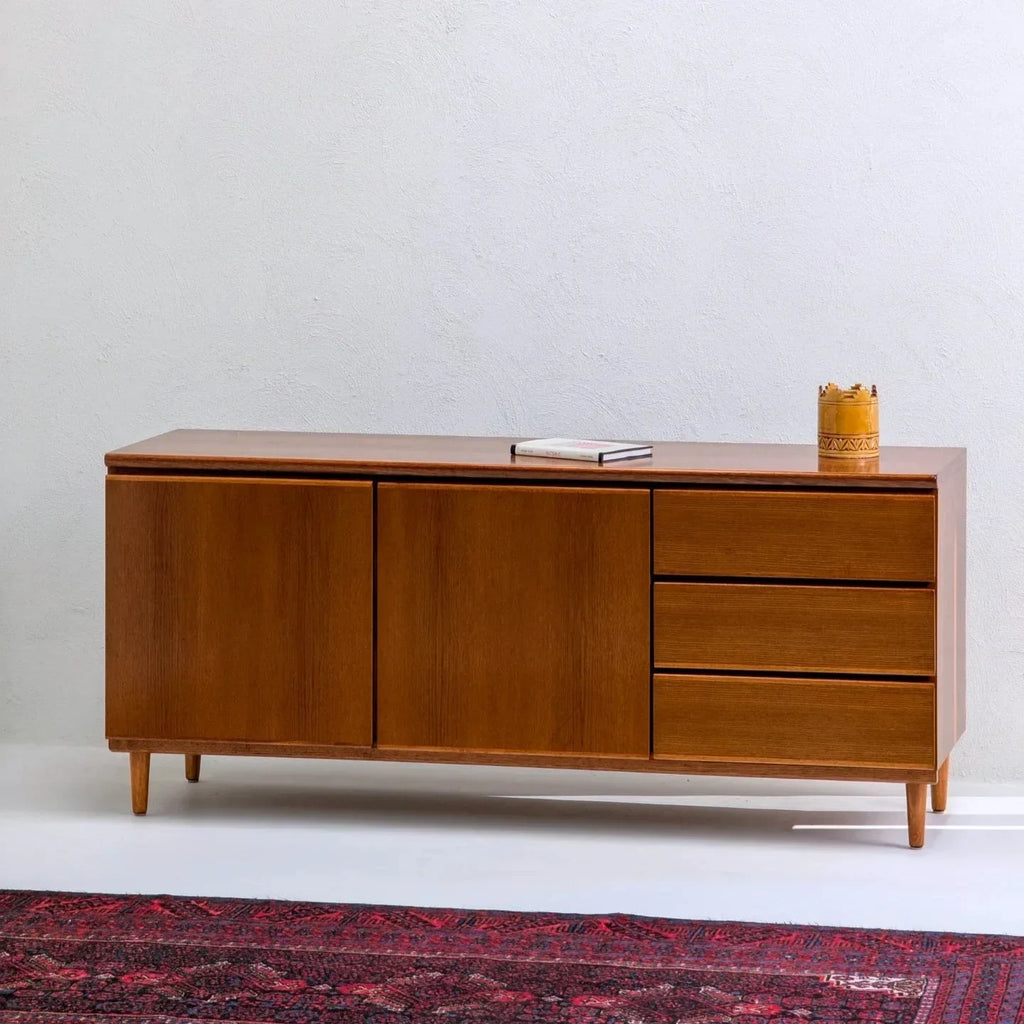 Mid-century teak sideboard with three drawers, cabinet doors, and decor on top