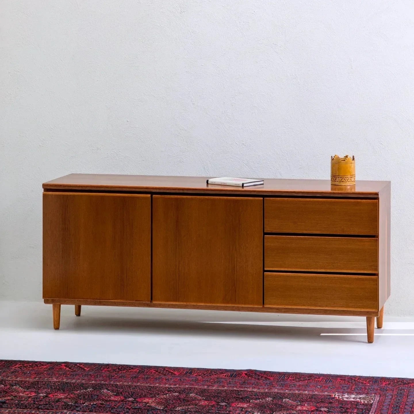 Mid-century teak sideboard with three drawers, cabinet doors, and decor on top