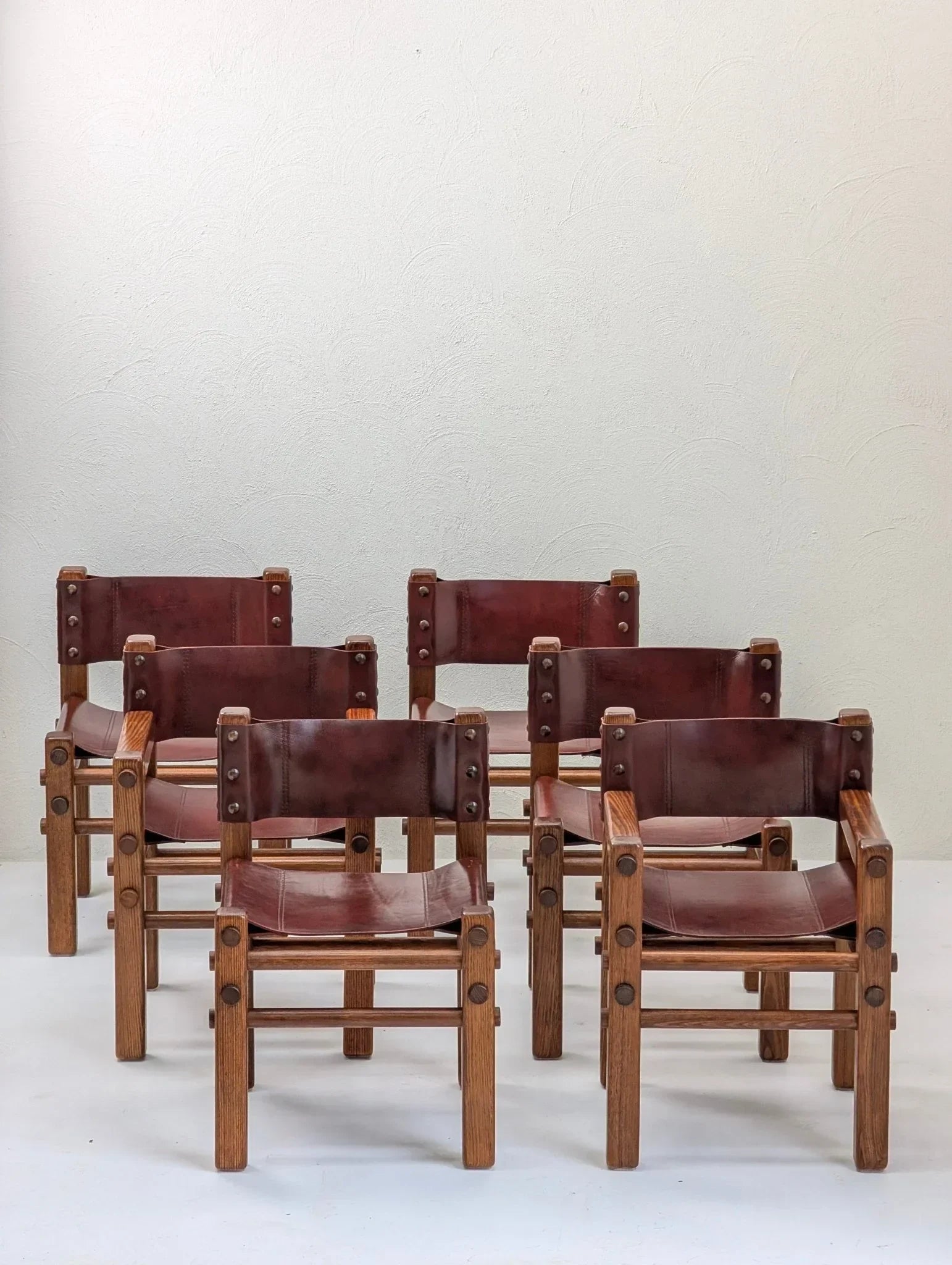 Set of six vintage 1970s brown leather and wood dining chairs against a plain wall