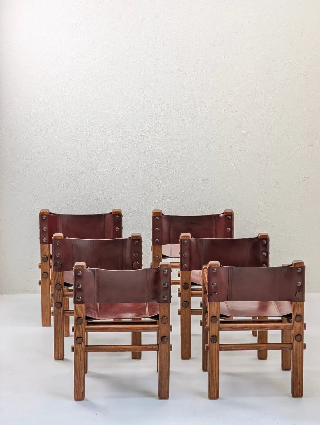 Set of six vintage 1970s leather and wood dining chairs against a plain wall