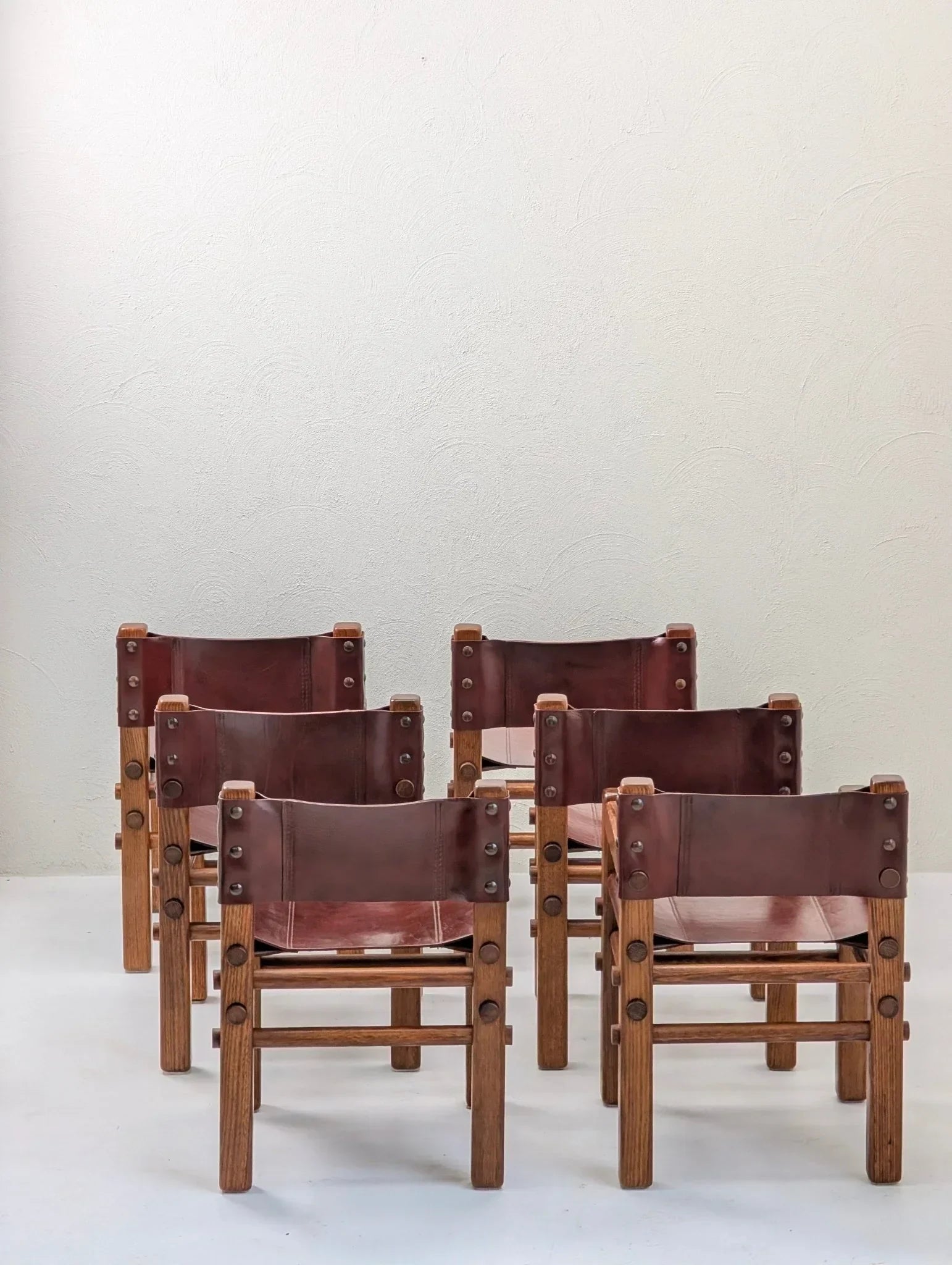 Set of six vintage 1970s leather and wood dining chairs against a plain wall