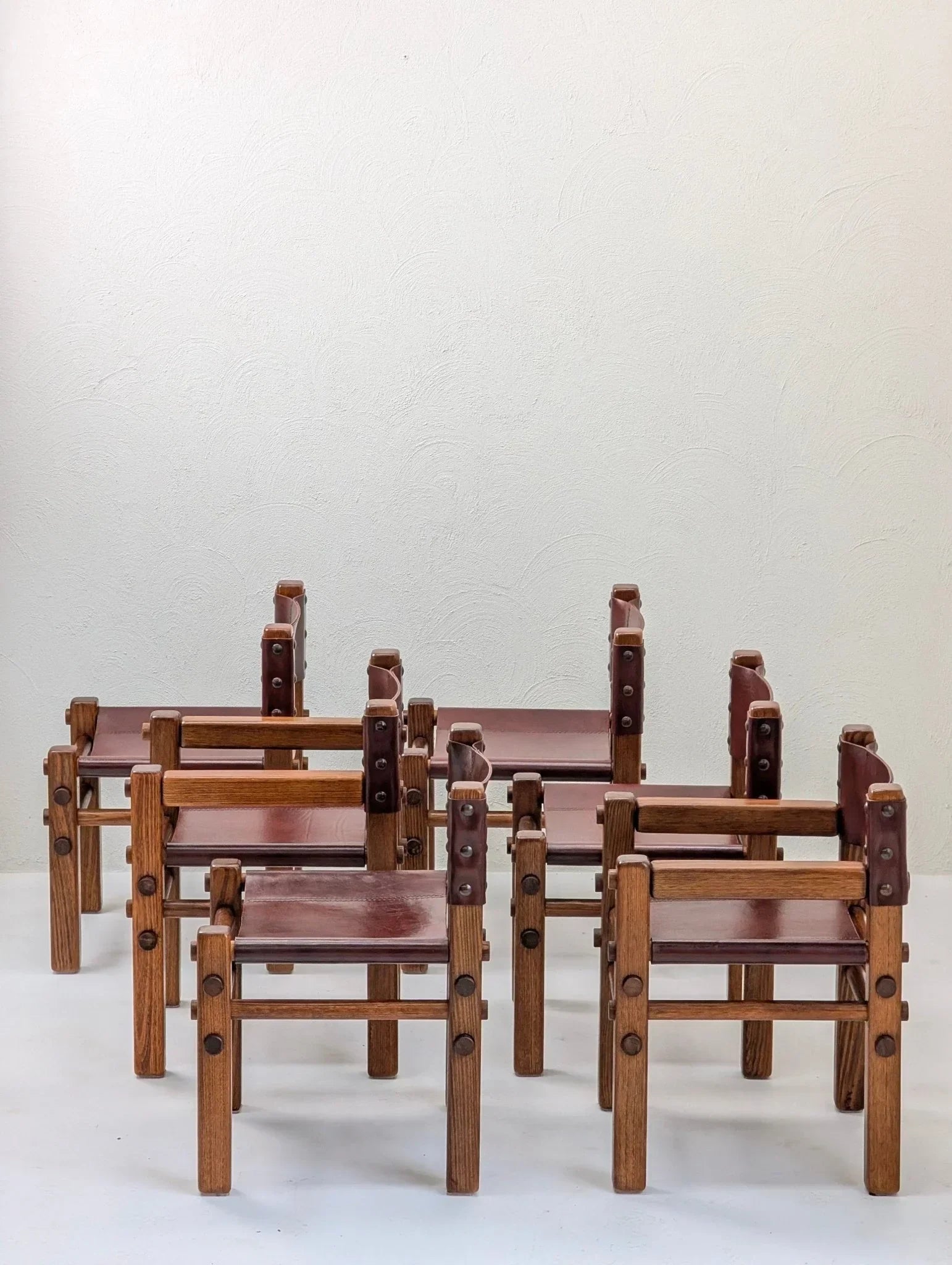 Set of six vintage 1970s oak and brown leather dining chairs against plain wall