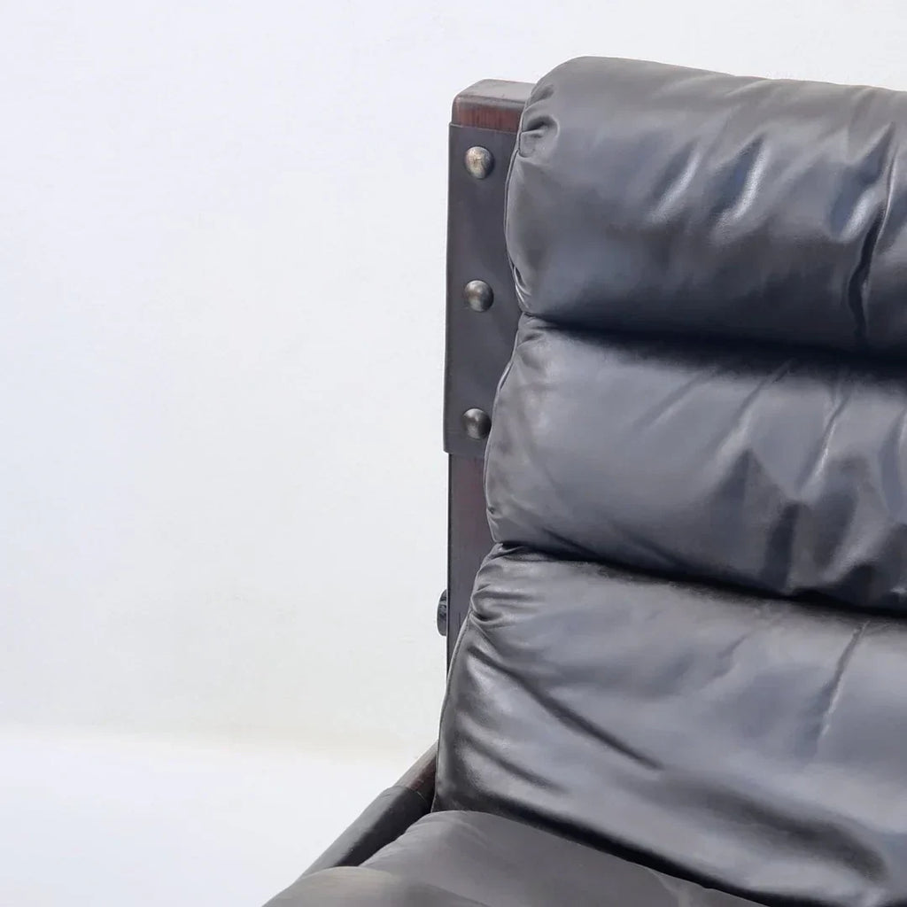 Close-up of black leather cushion lounge chair with dark wood frame and visible metal bolts