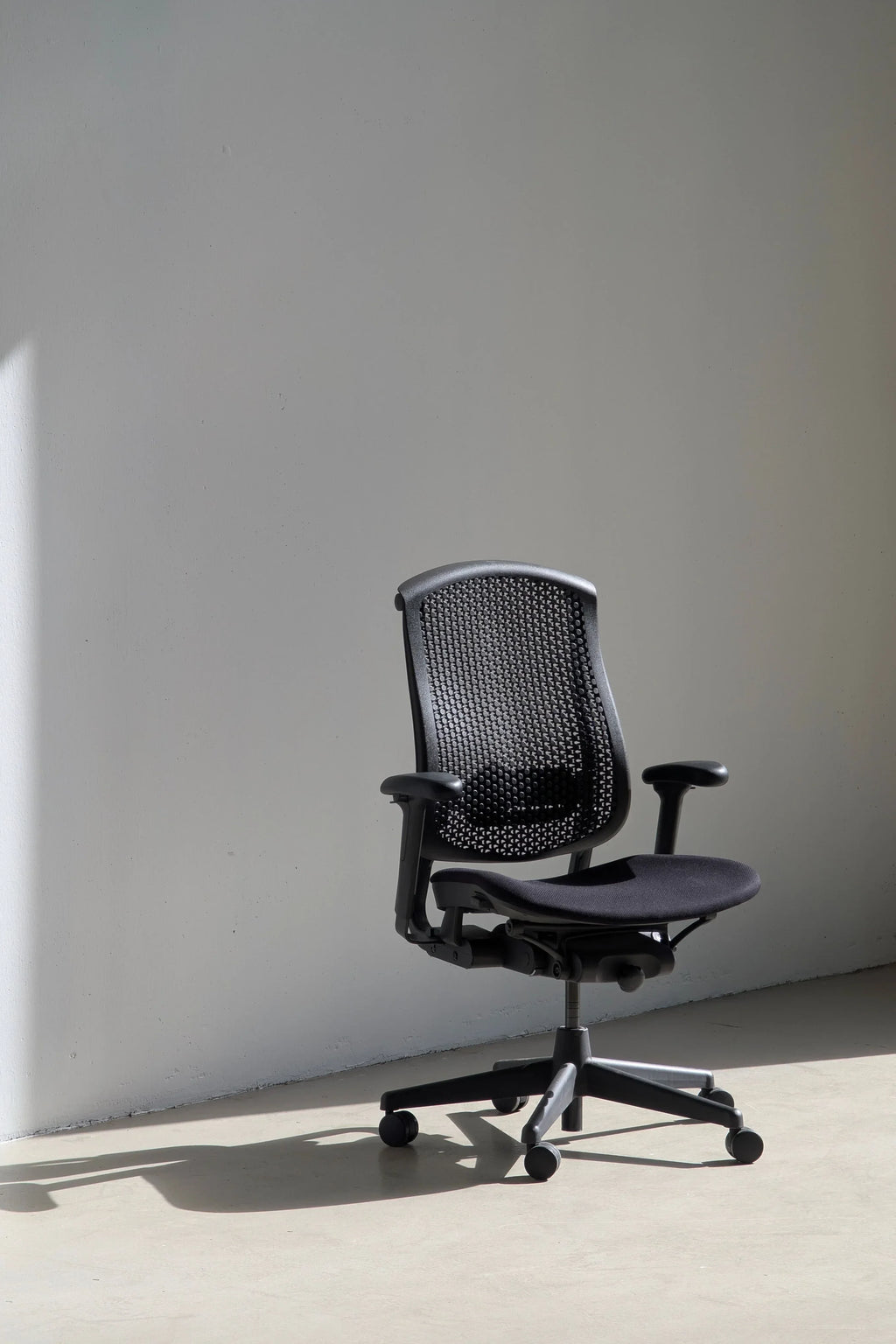 Black ergonomic office chair with mesh backrest in minimalist room with sunlight