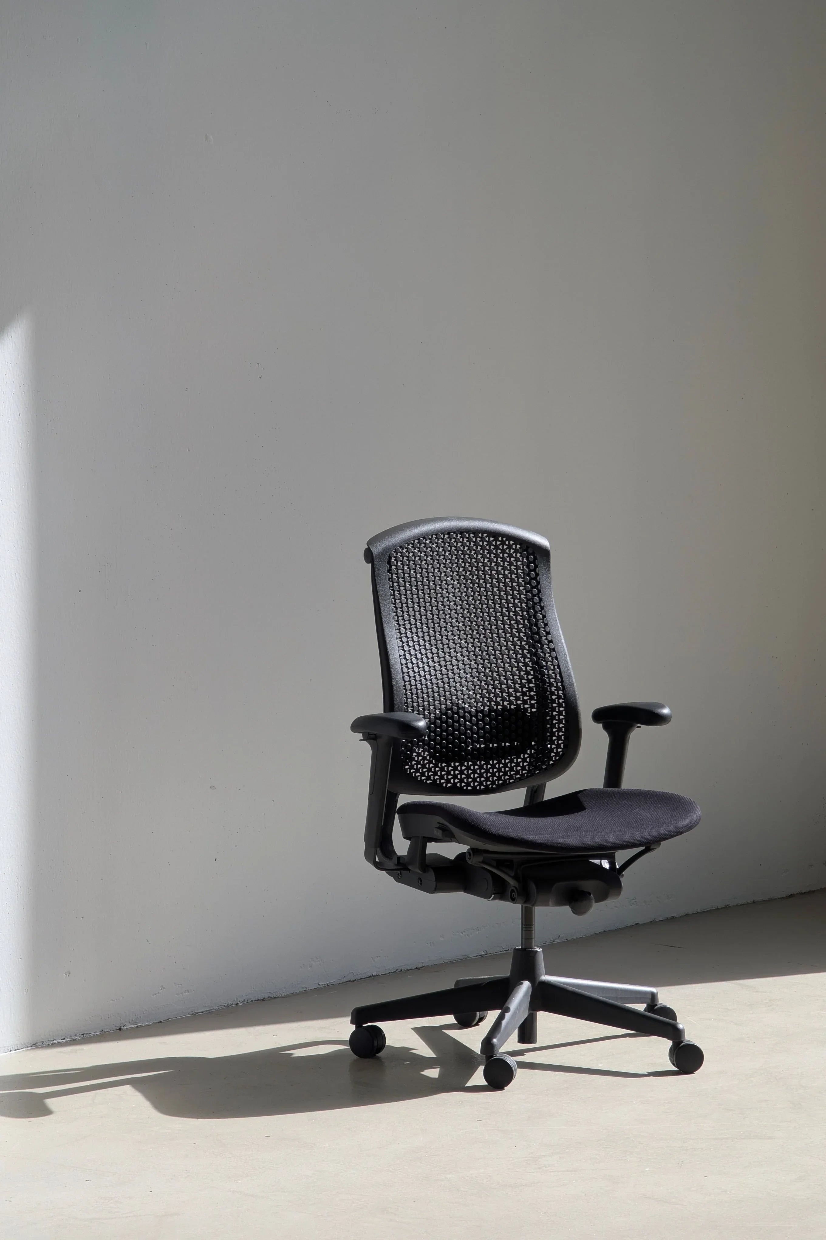 Black ergonomic office chair with mesh backrest in minimalist room with sunlight