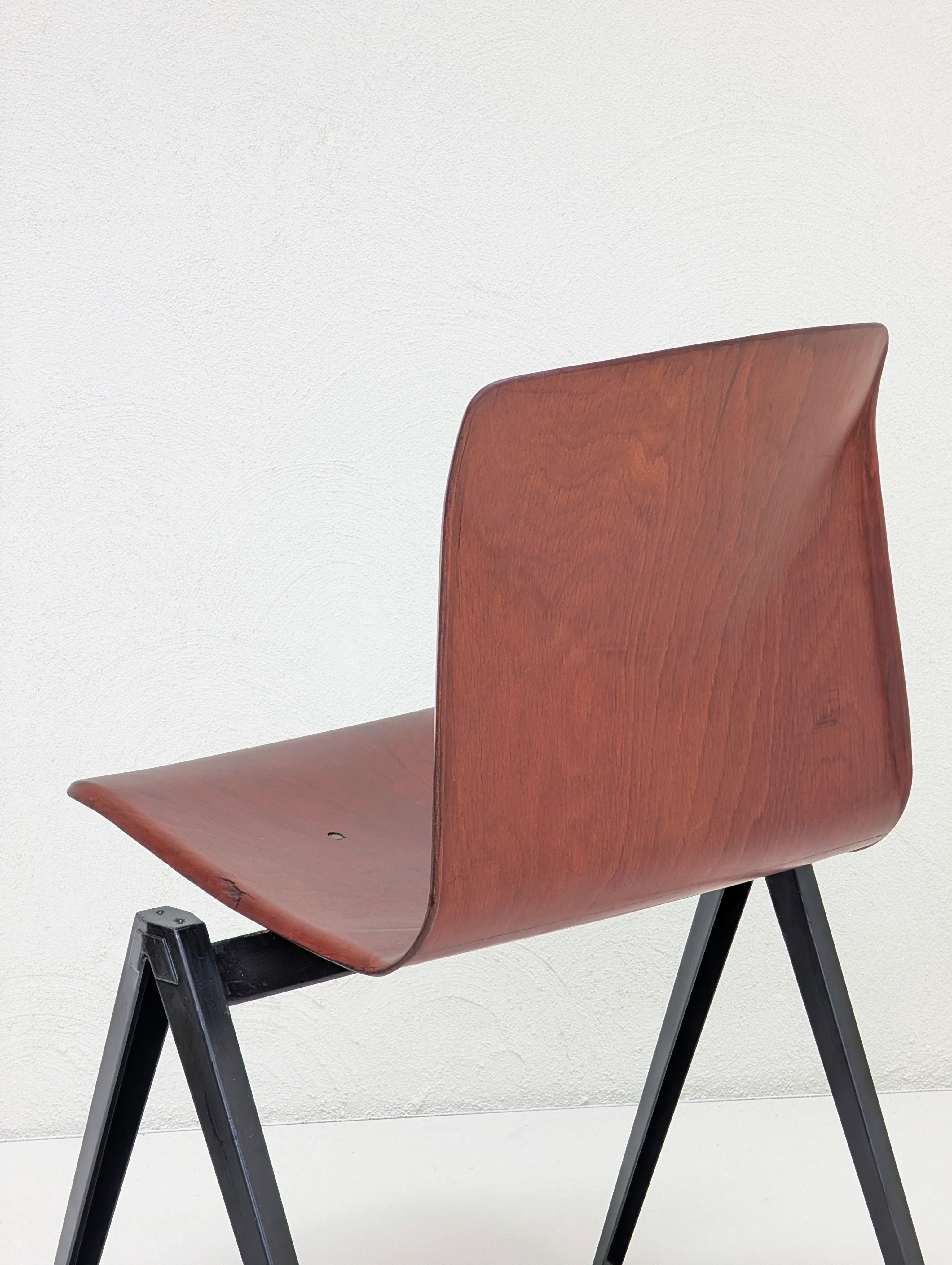 Minimalist chair with curved wooden seat and black metal angled legs against white wall