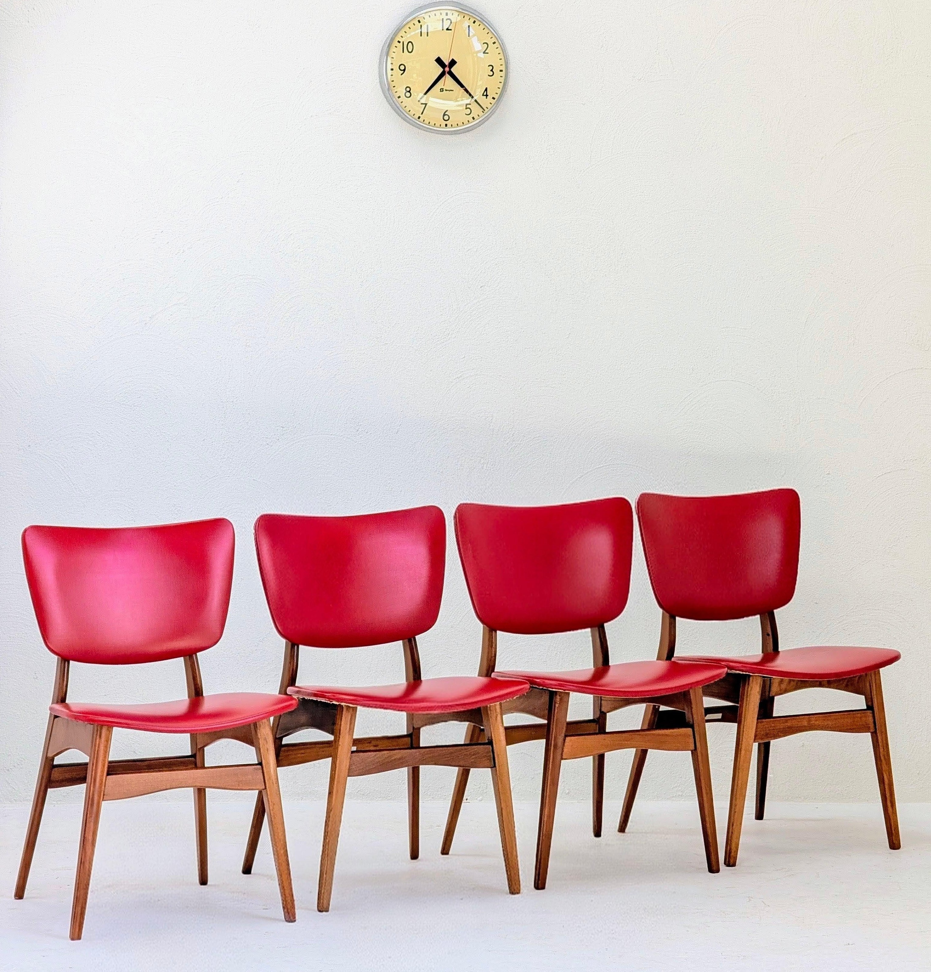 Four red mid-century modern chairs under a vintage wall clock on a white background
