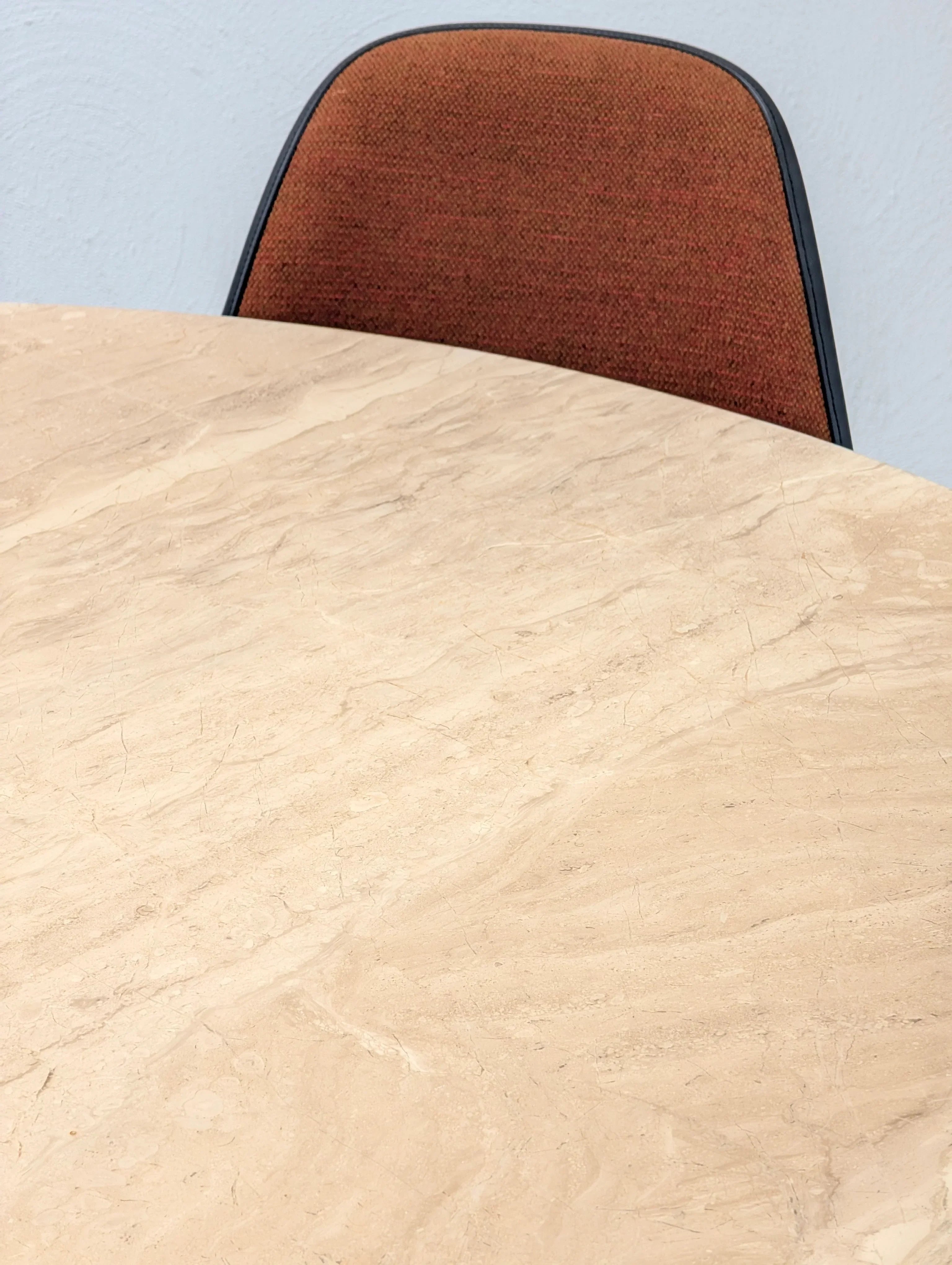 Beige marble table with a brown upholstered chair in a minimalist setting