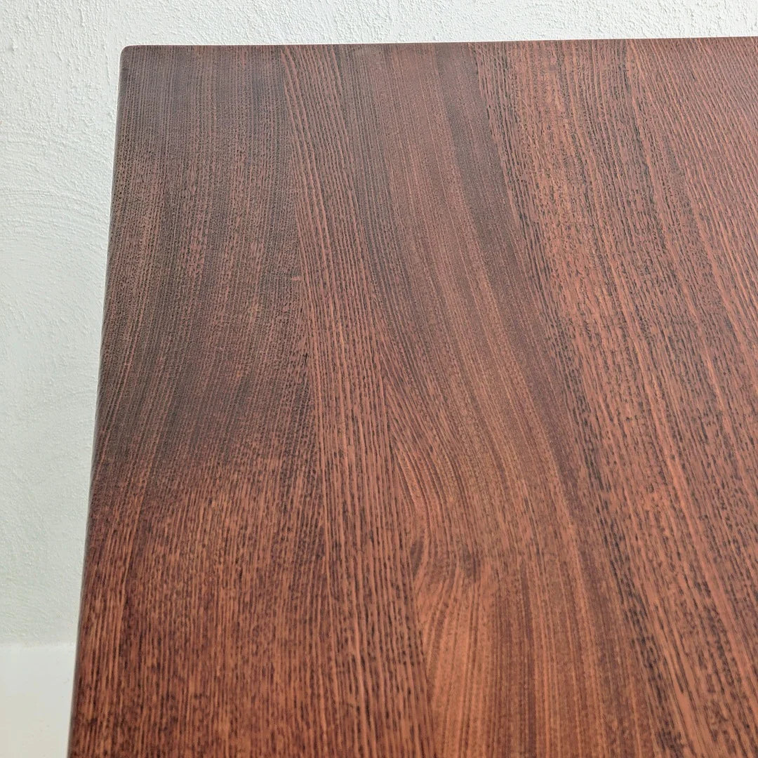 Close-up of dark wooden tabletop with textured wood grain pattern against white wall