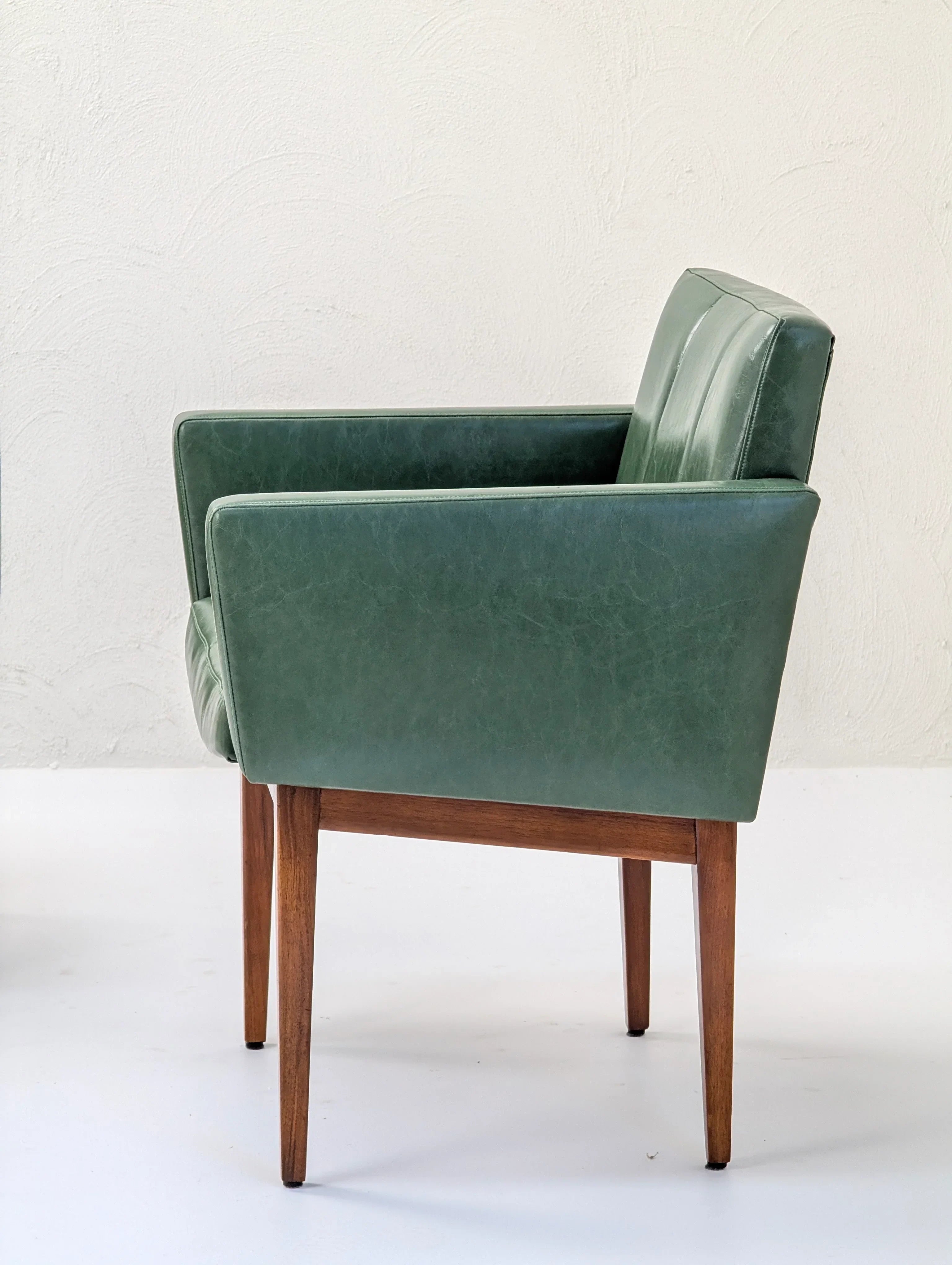 Green mid-century modern armchair with wooden legs against a white textured wall