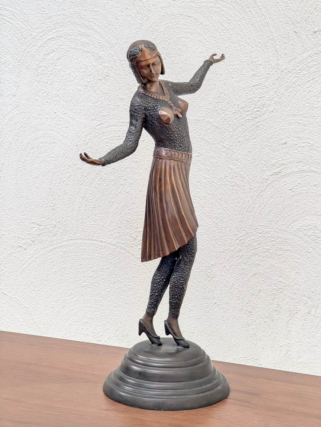 Bronze sculpture of a female figure in a pleated skirt and textured top on a round base