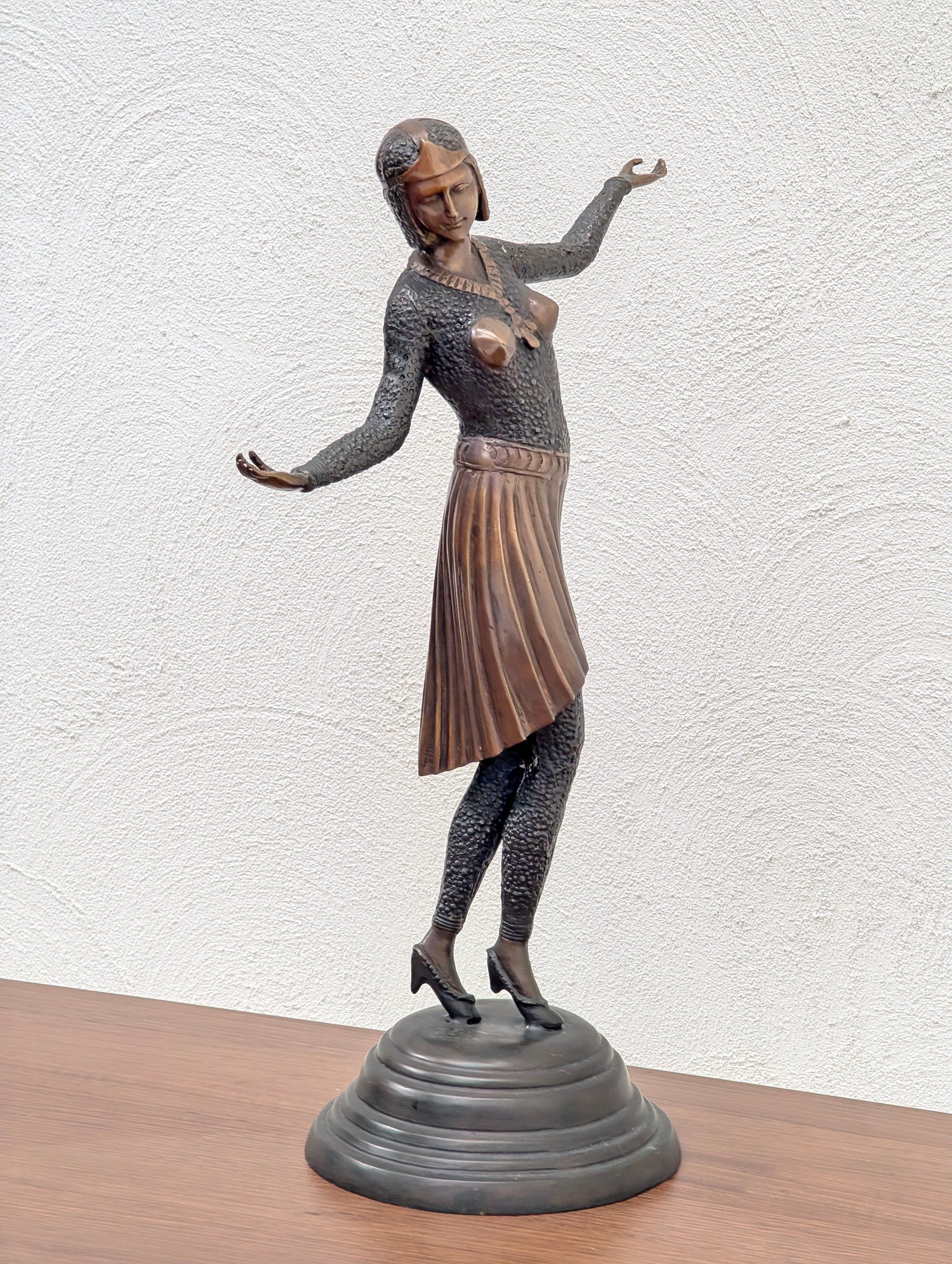 Bronze sculpture of a female figure in a pleated skirt and textured top on a round base