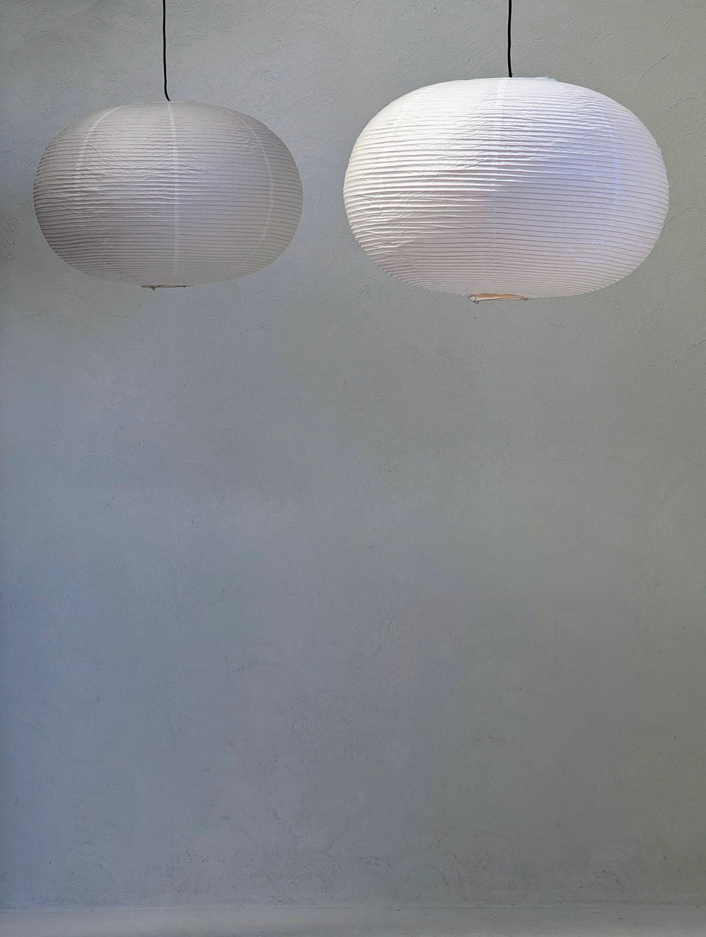 Two round white paper lantern pendant lights hanging against a plain gray wall.