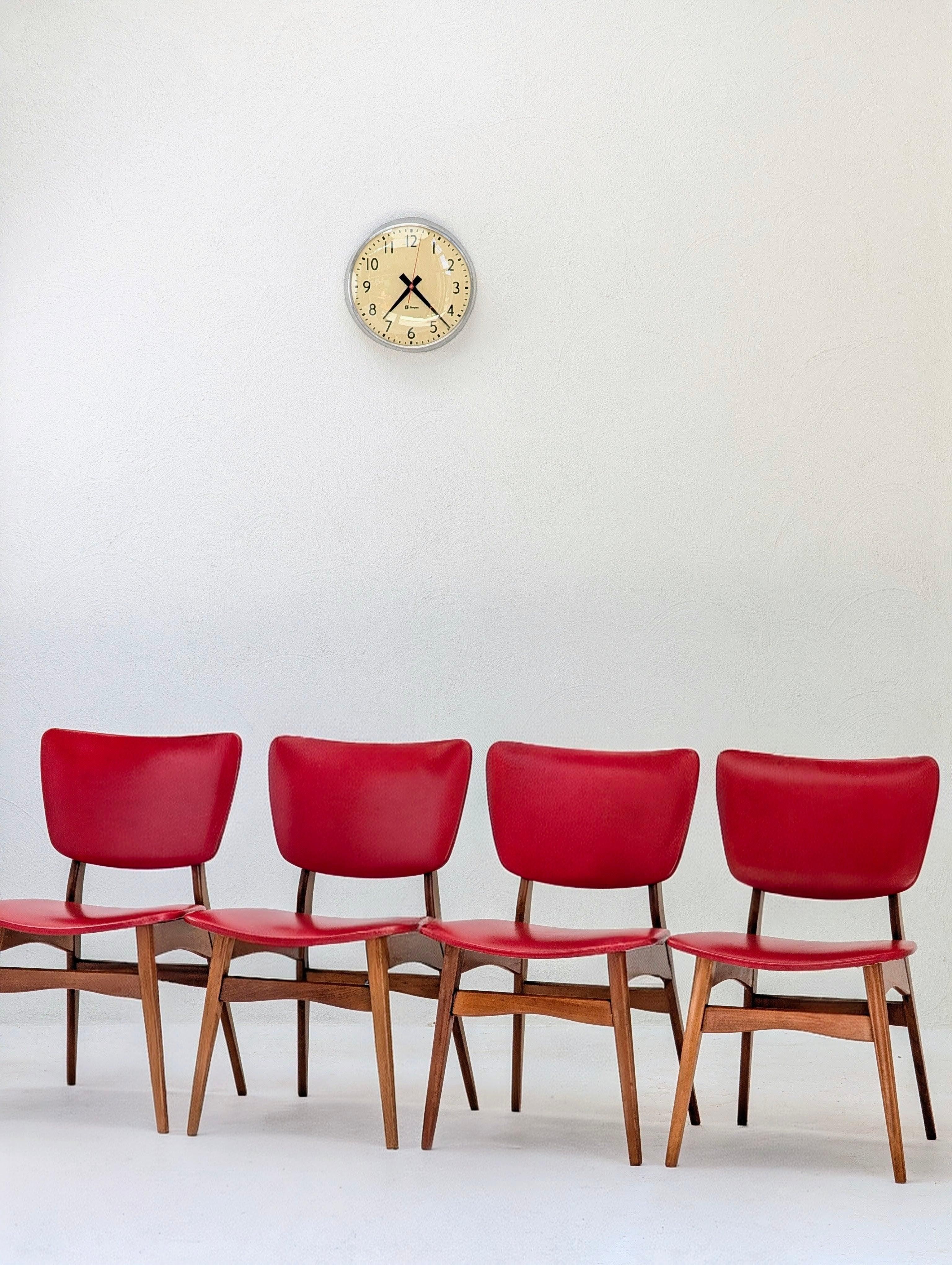 Four red vintage chairs in a row under a retro wall clock on a white background