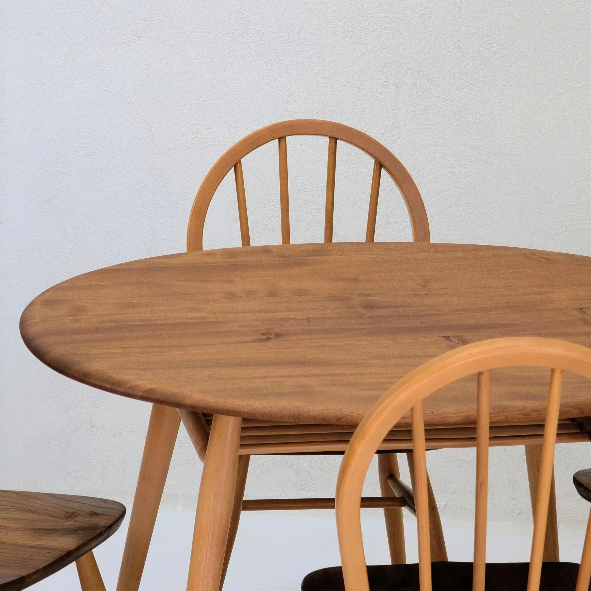 Round wooden dining table with matching spindle back chairs against a light wall