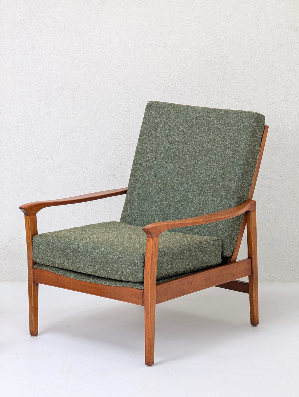Mid-century modern wooden armchair with olive green upholstered cushions against white wall