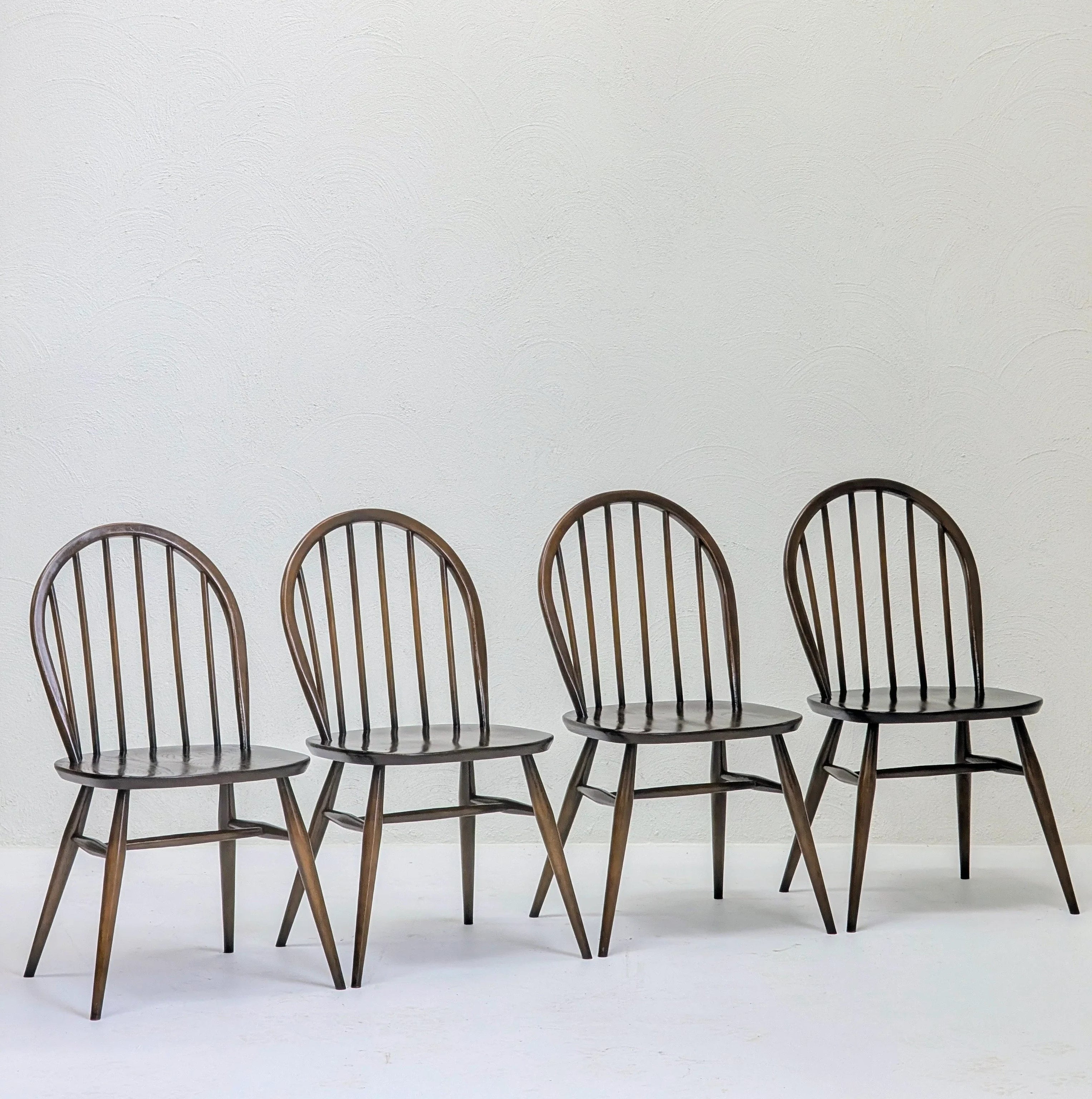 Four dark wooden spindle-back chairs arranged in a row against a plain white textured wall