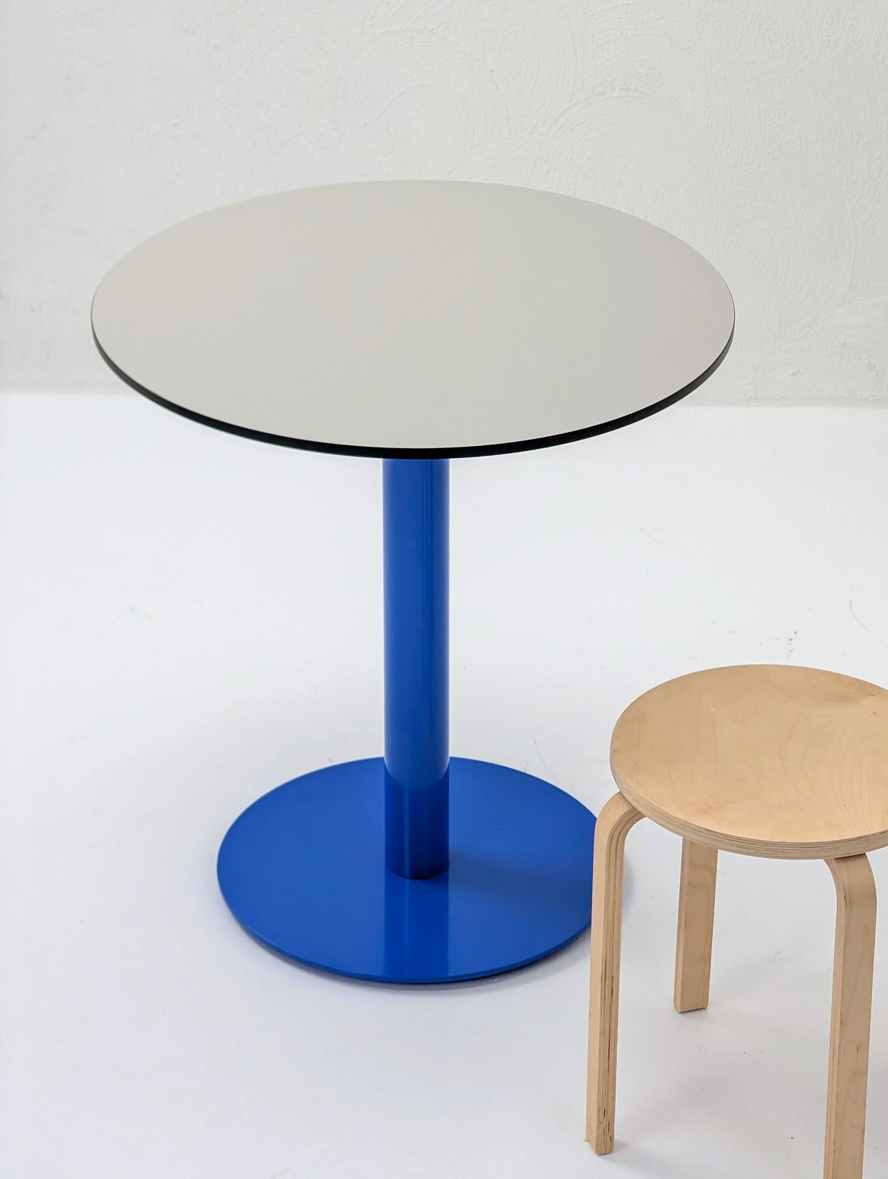Modern round table with blue base and light wood stool on white background