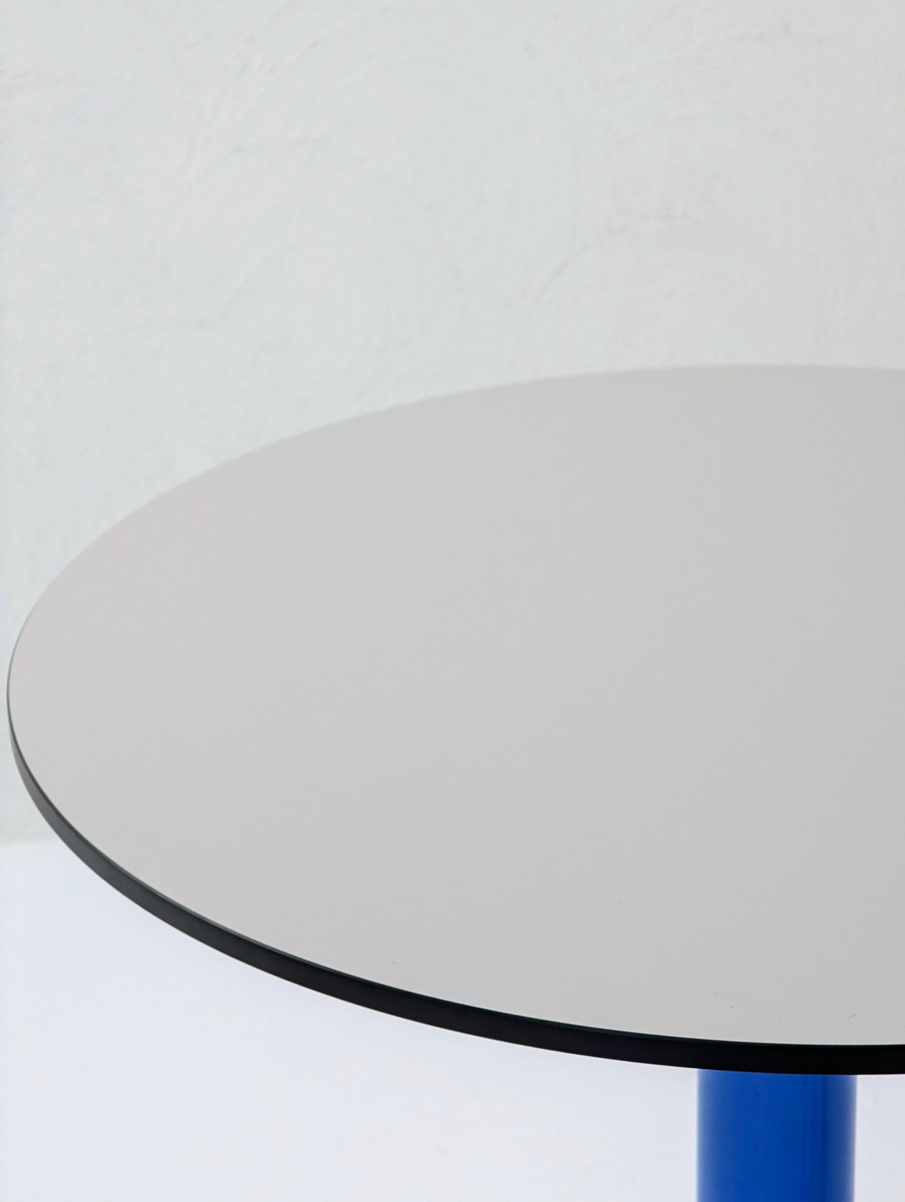Modern round table with white top, black edge, and blue cylindrical leg on a light background