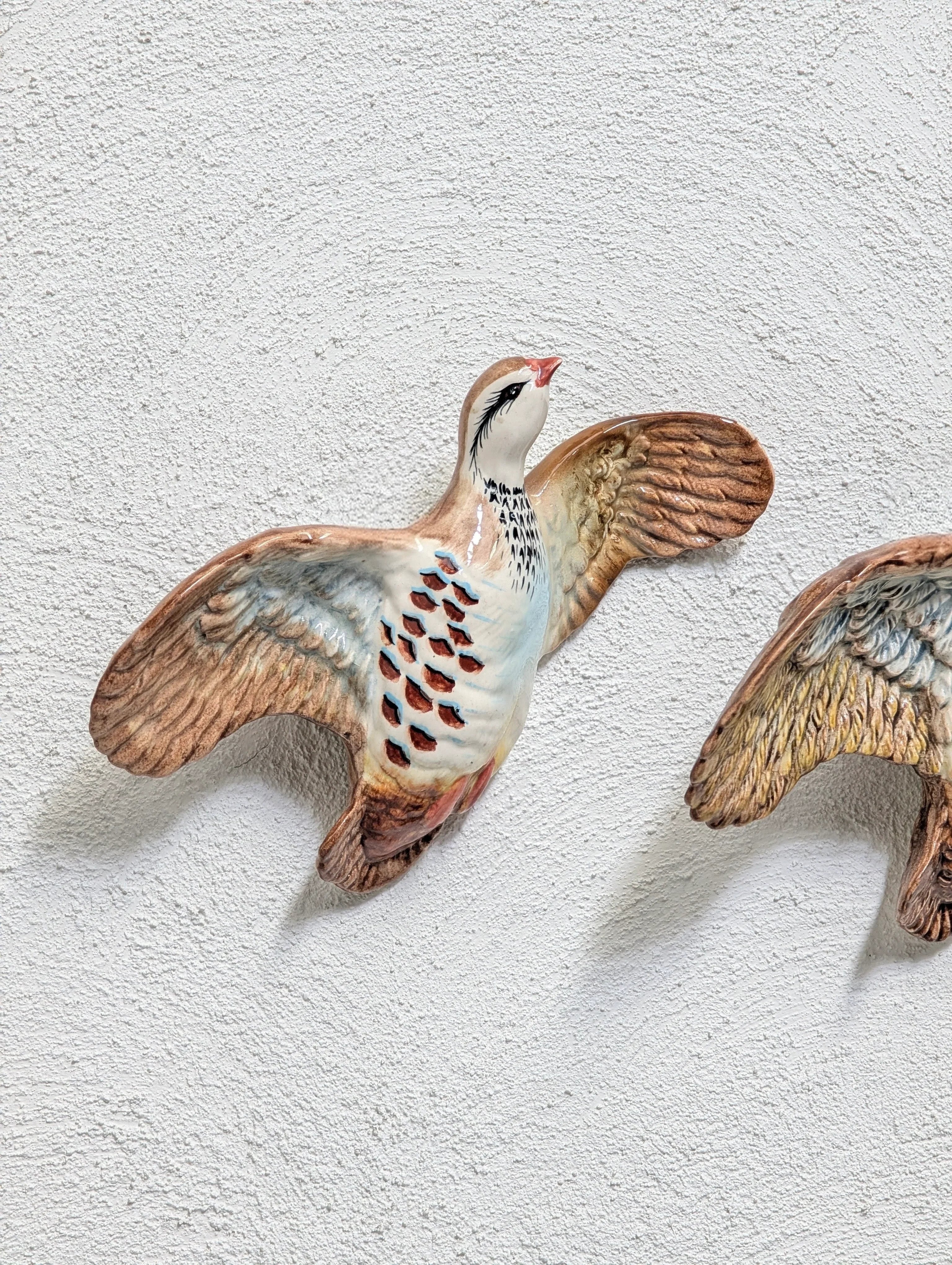 Ceramic bird wall decoration with brown, white, and blue feathers on a white textured wall