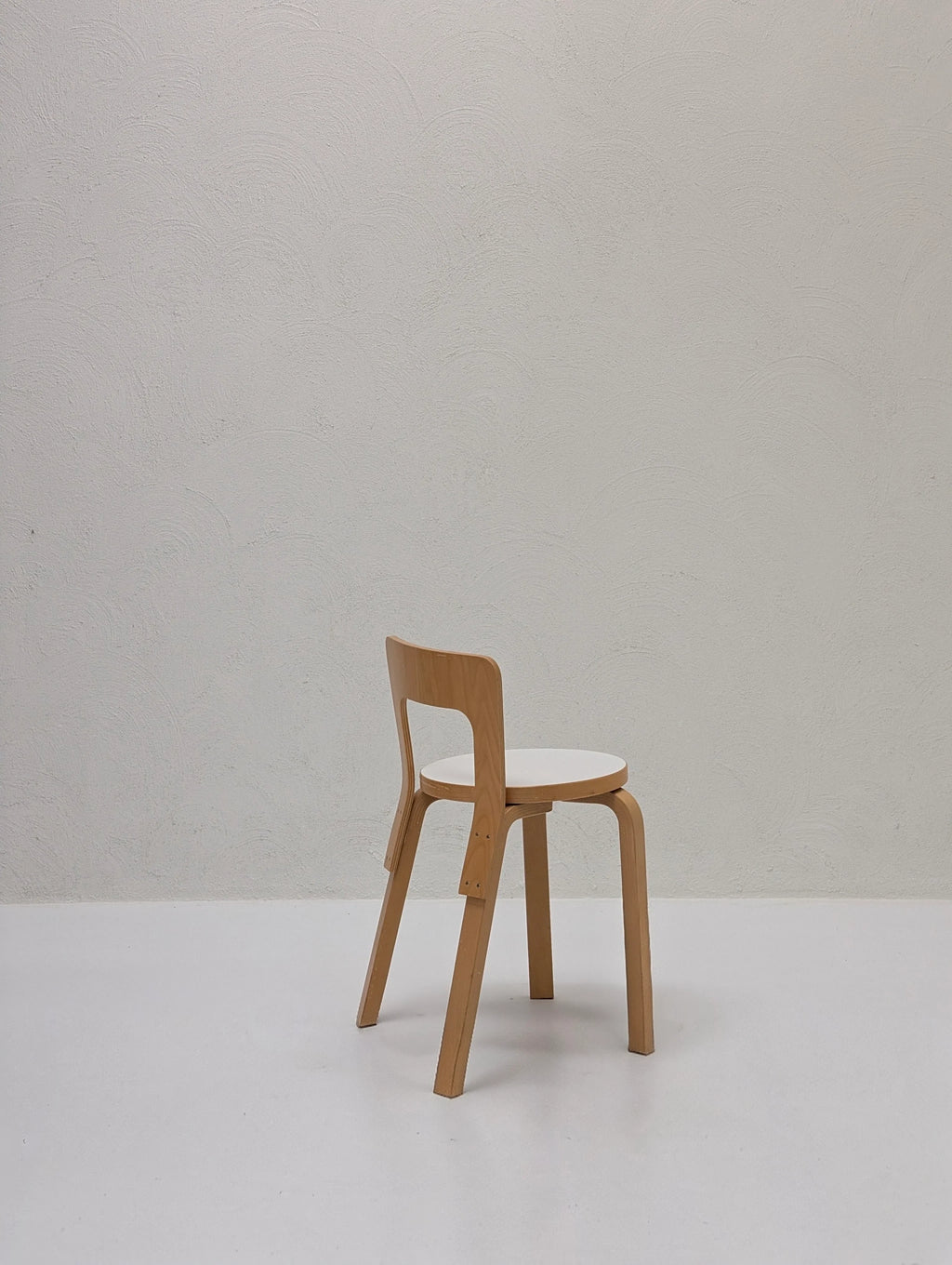 Minimalist wooden chair with white seat in empty room with textured white wall