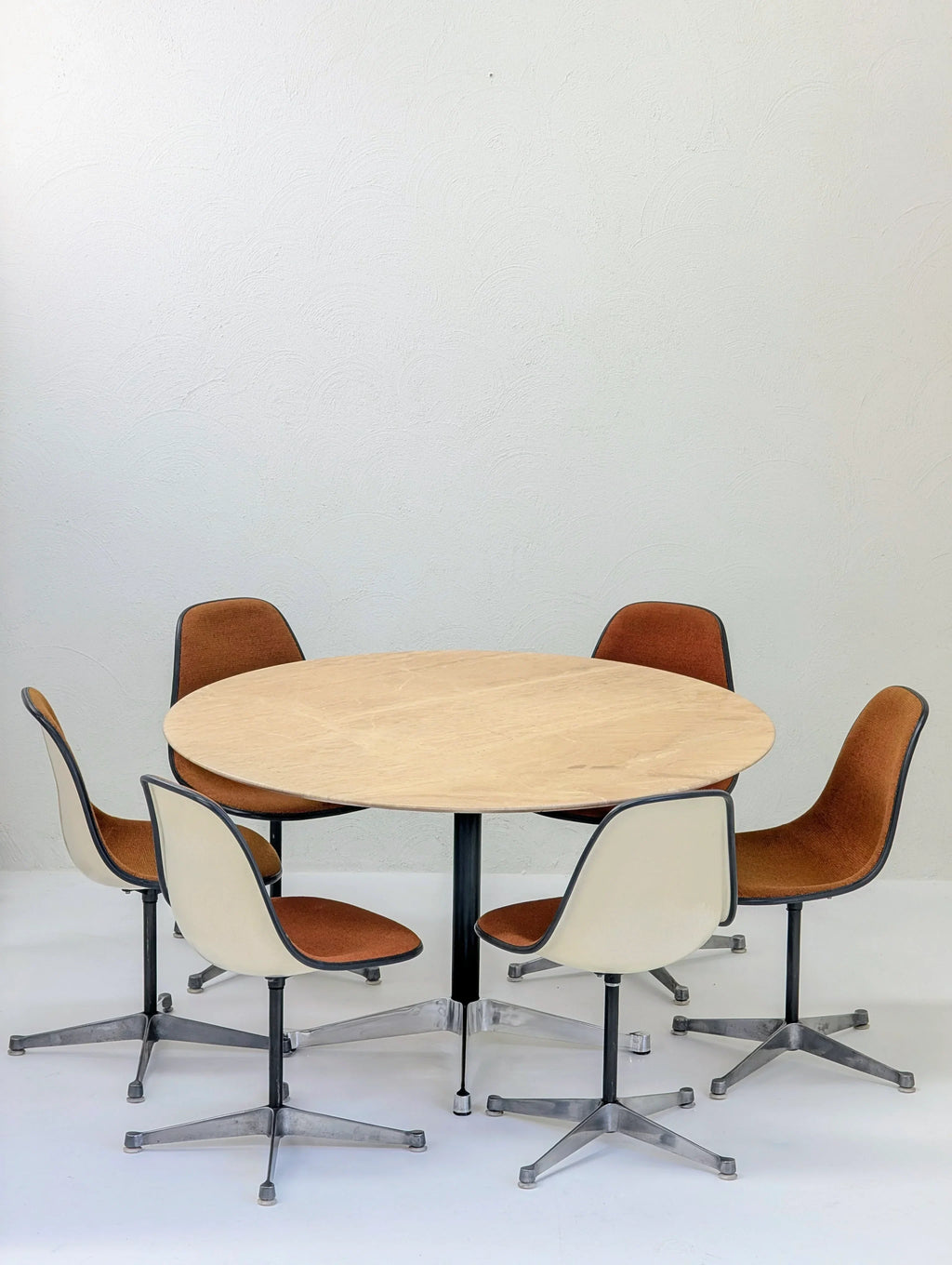 Round wooden table with five vintage brown swivel chairs in a minimalist room
