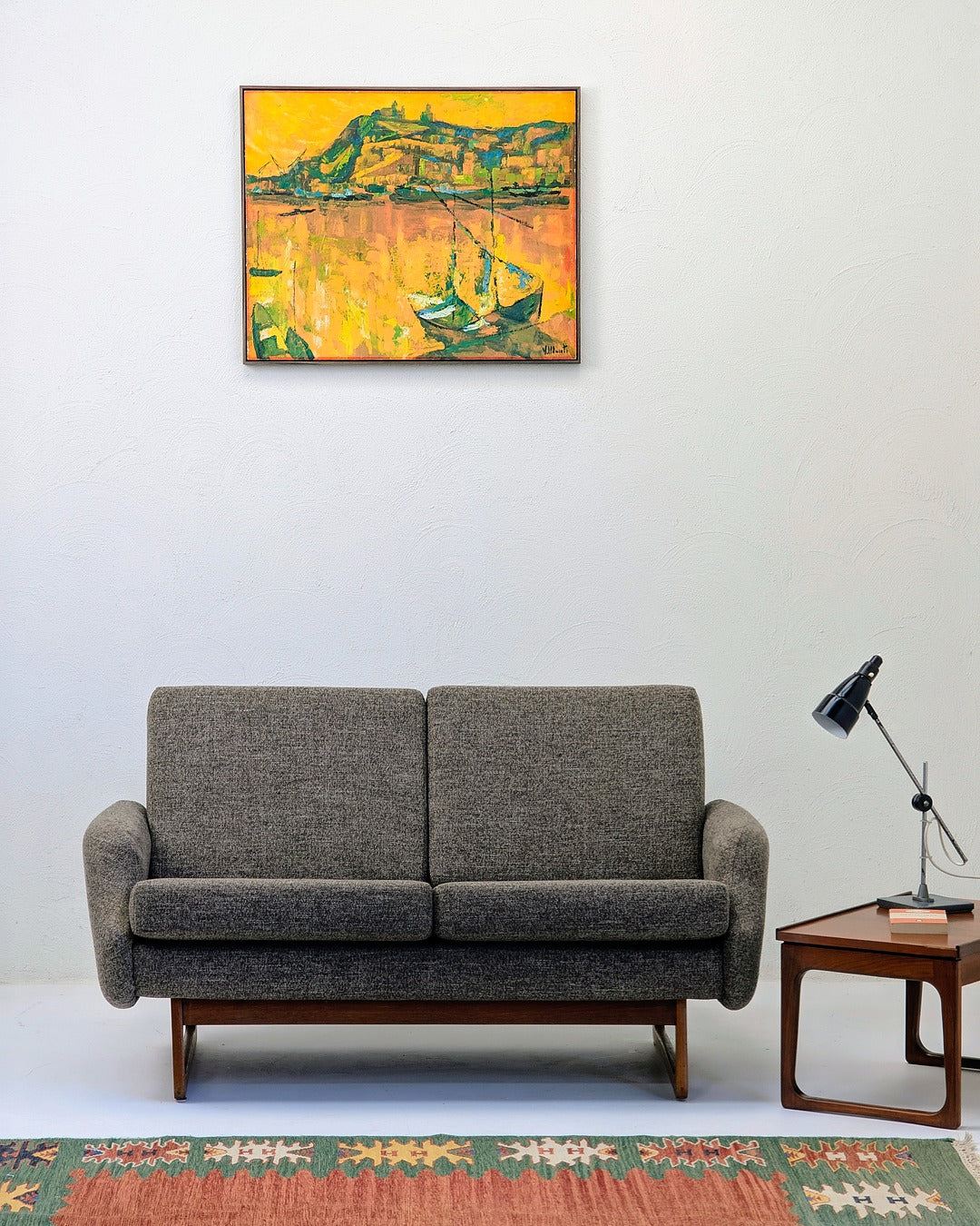 Modern living room with gray fabric sofa, wooden side table with black lamp, colorful rug, and yellow boat painting