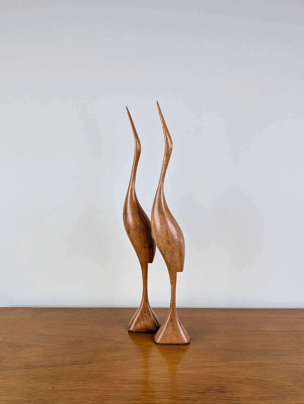 Pair of carved wooden crane sculptures on a wooden surface against a plain background