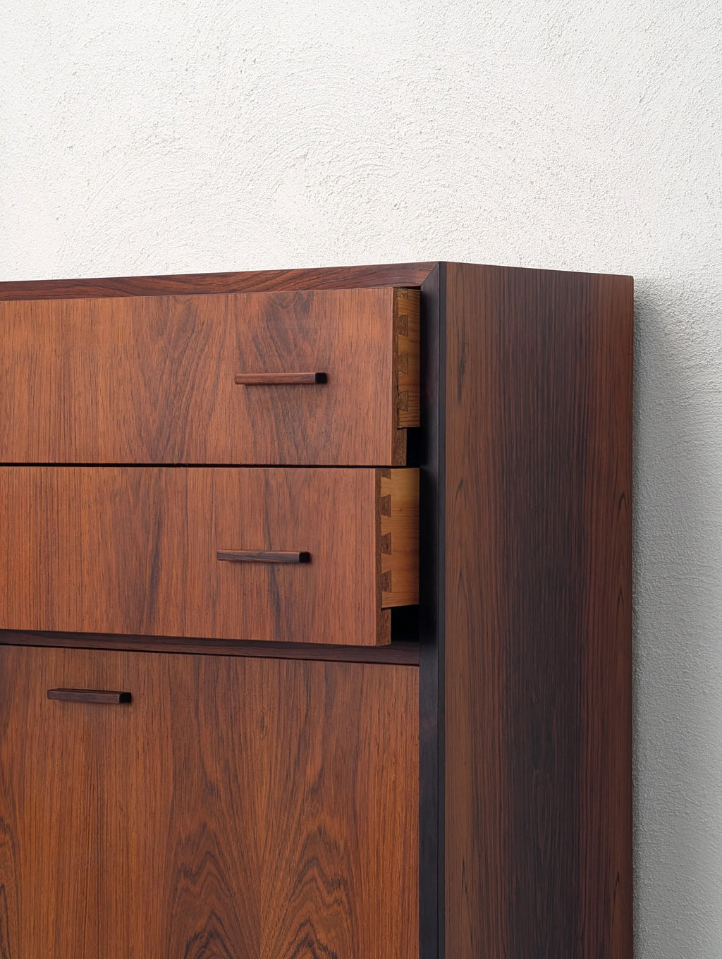 Mid-century modern rosewood dresser with open dovetail drawer against a white wall