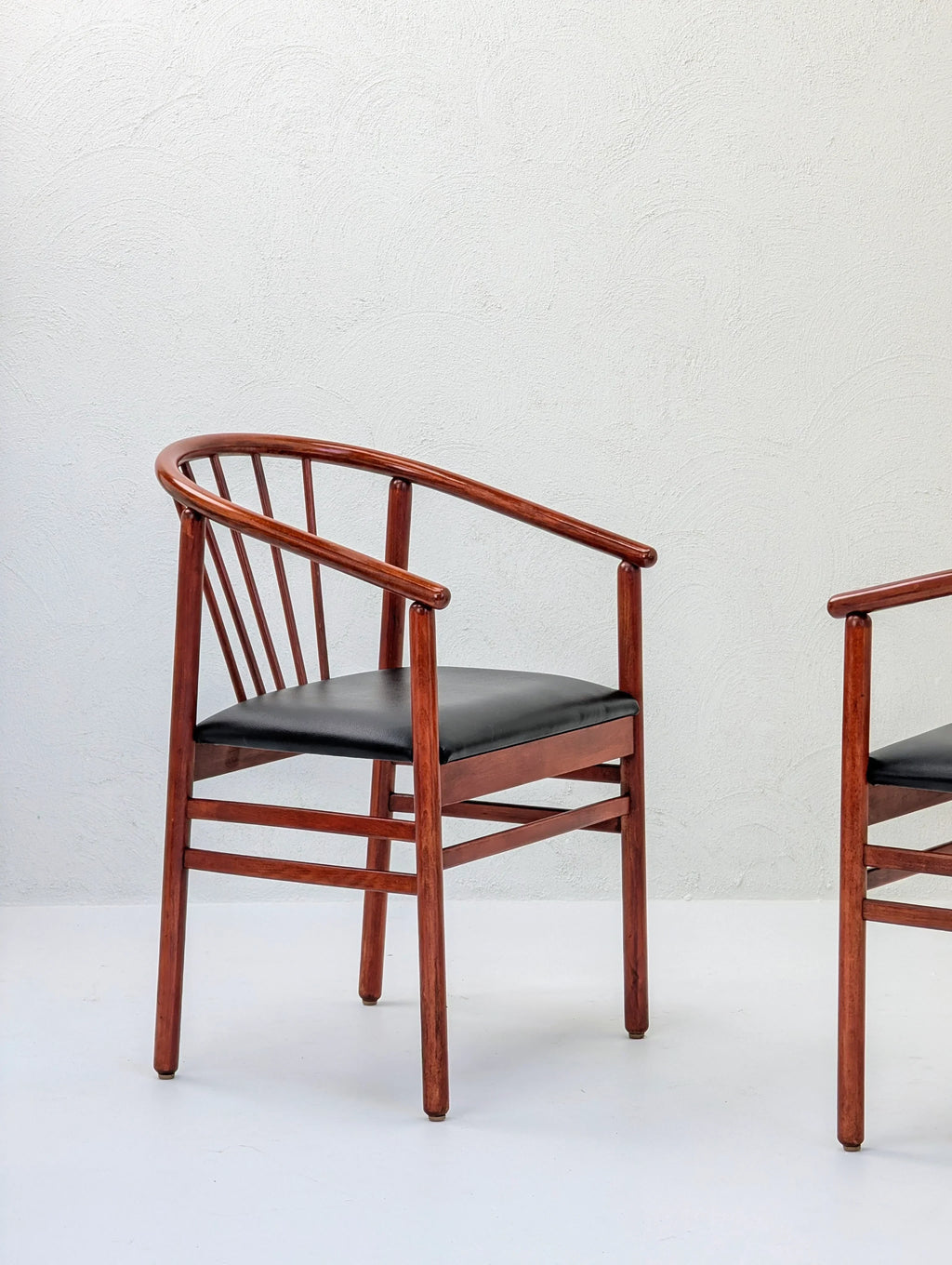 Wooden dining chair with curved backrest and black cushion seat against white wall