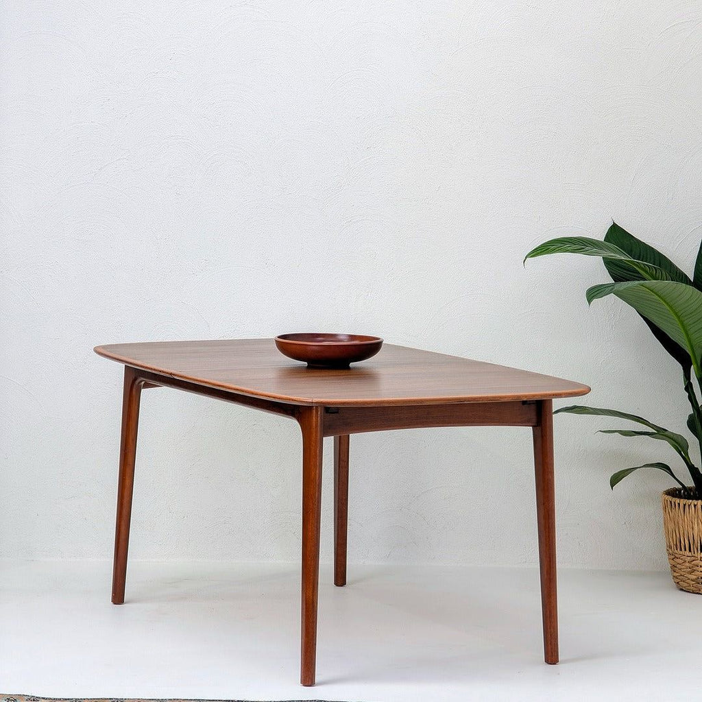 Mid century modern wooden dining table with bowl, potted plant, white textured wall