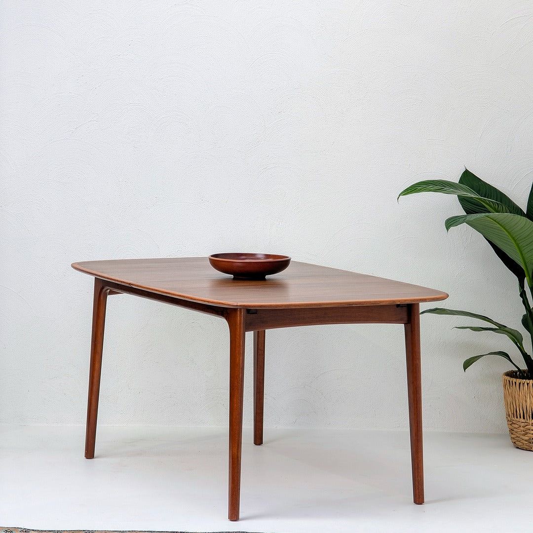 Mid century modern wooden dining table with bowl, potted plant, white textured wall